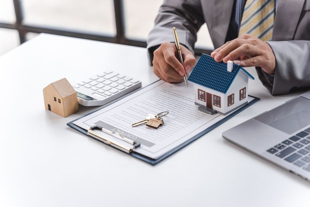 A man is signing a contract with a model house on a clipboard.