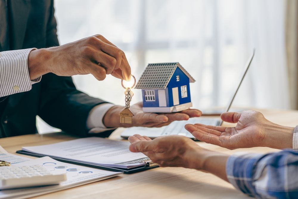 A man is giving a key to a woman while holding a model house.