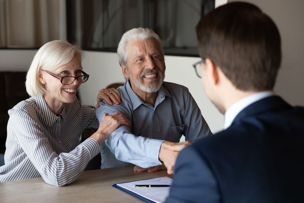 An elderly couple is shaking hands with a man while sitting at a table.