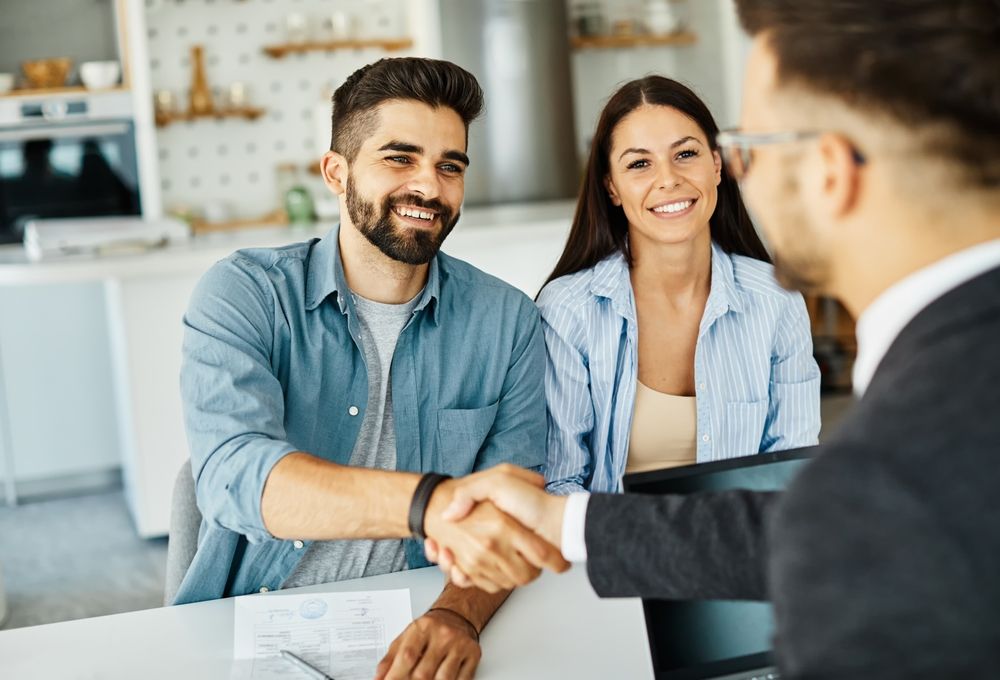 A man and woman are shaking hands with a real estate agent.