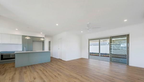 An Empty Living Room with Hardwood Floors and Sliding Glass Doors Leading to A Kitchen | Mid-North Coast, NSW | BDM Constructions