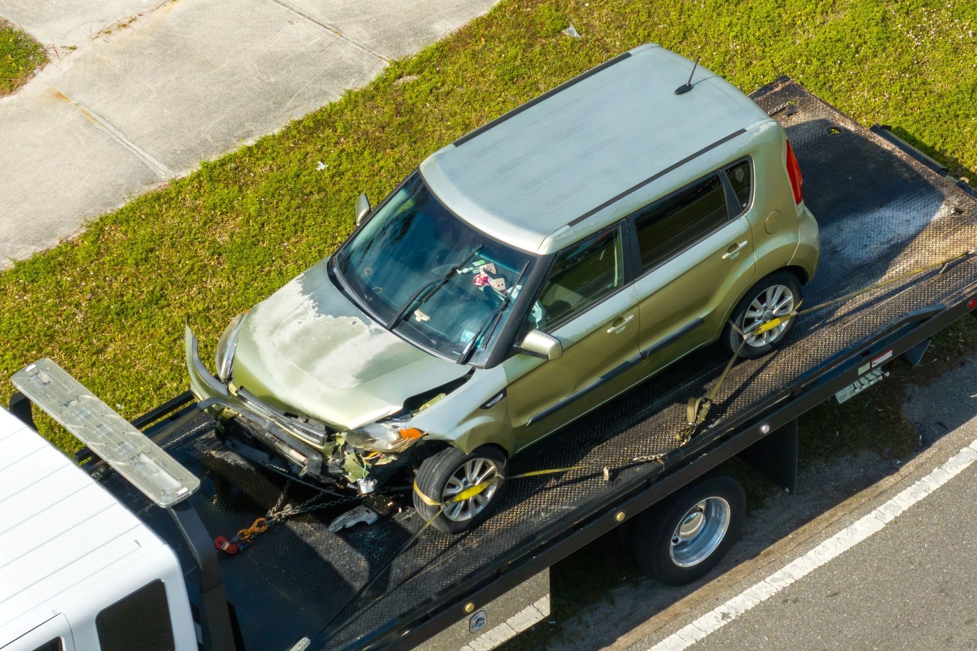 Damaged green Kia Soul on a tow truck. Front end severely damaged.