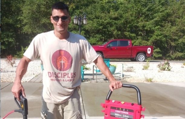 A man wearing a shirt that says disciples is standing next to a red truck.