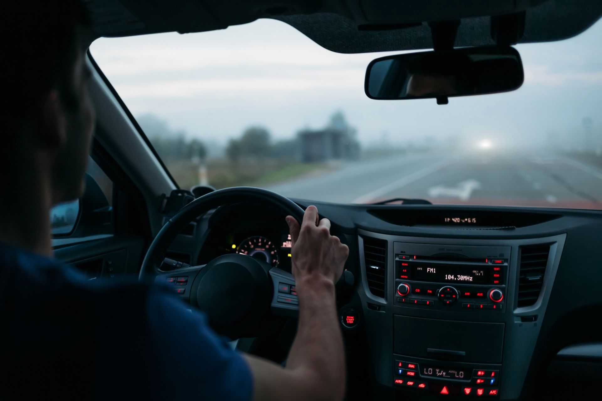 Persona conduciendo un automóvil en una carretera con niebla; interior del automóvil visible, faros en la distancia.