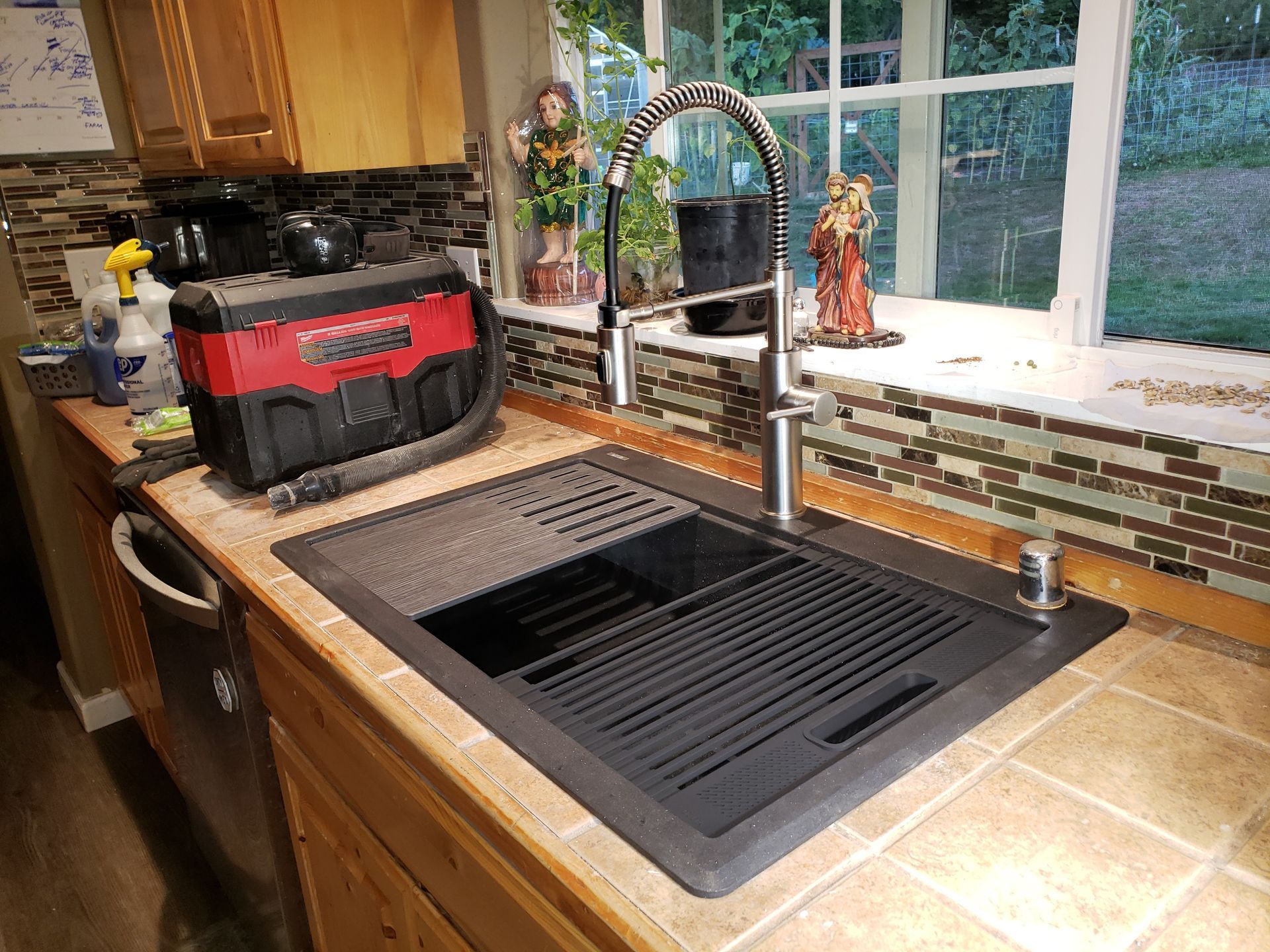 Kitchen sink and countertop with a black grill insert, red toolbox, and window view