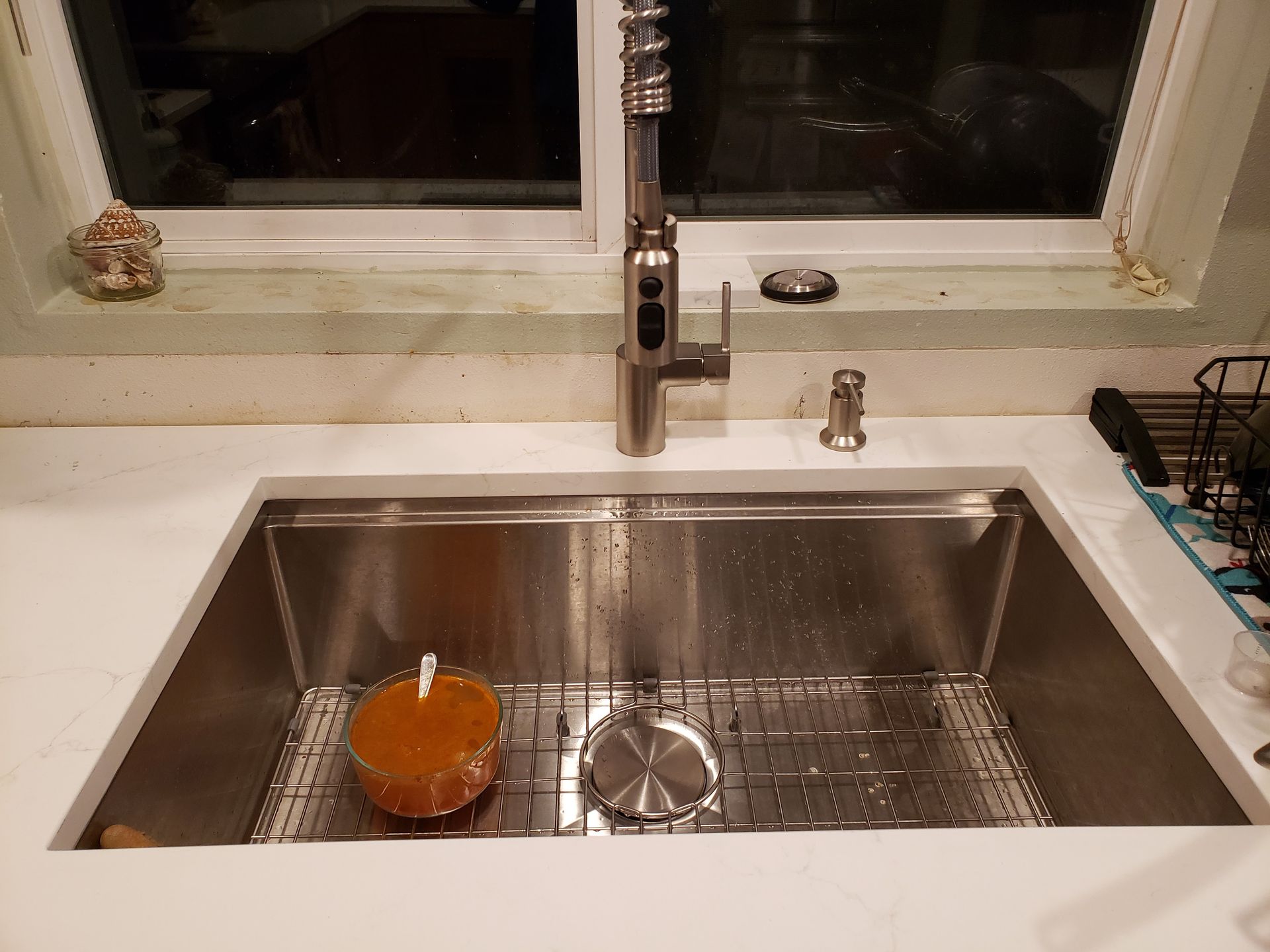 Kitchen sink with a stainless steel basin, orange dish, and faucet under a window.