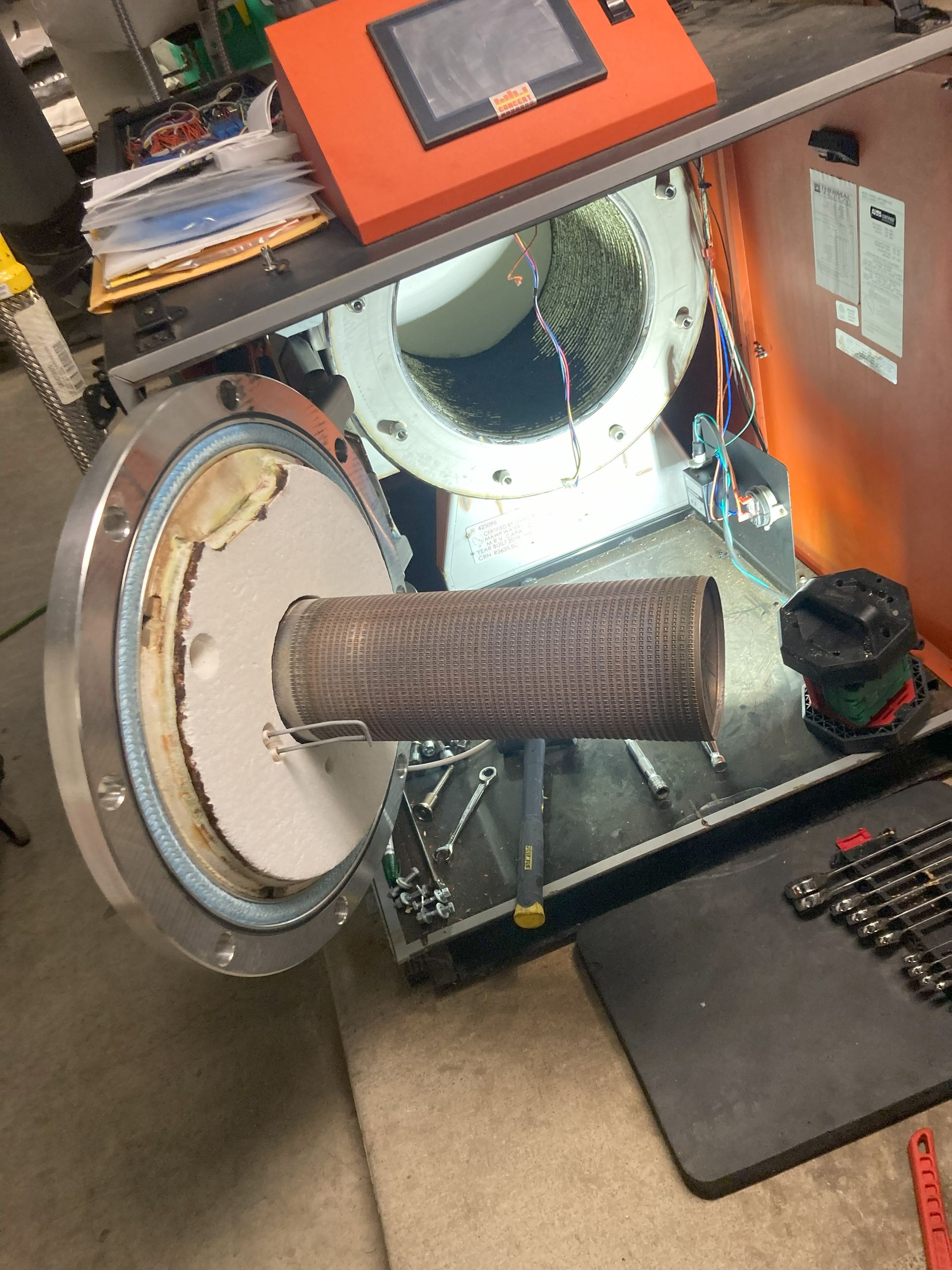Open dryer drum with a dusty hose extending out, inside an orange repair machine setup.