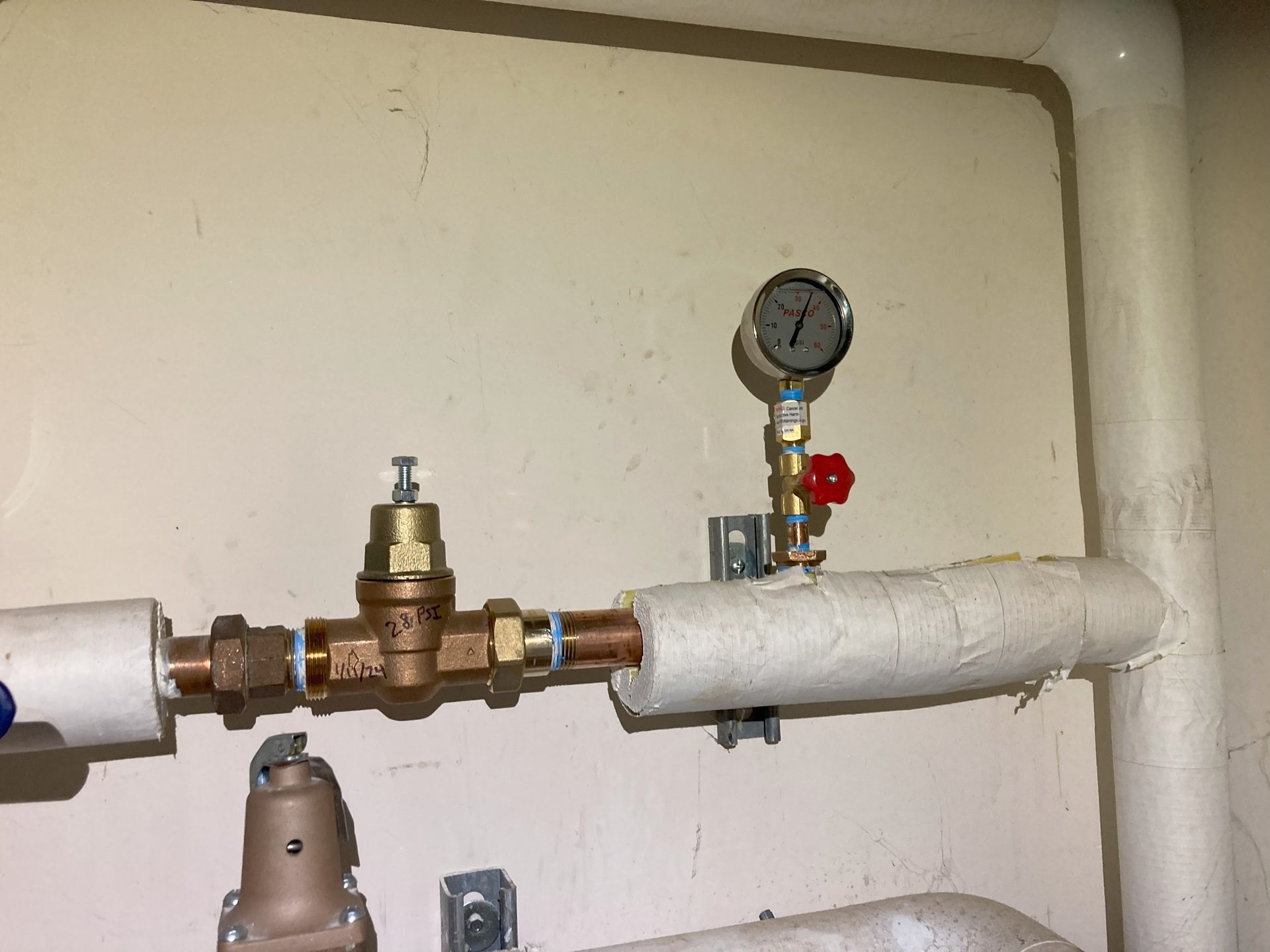 Pipes with pressure gauge and valve wrapped in white insulation inside a utility room