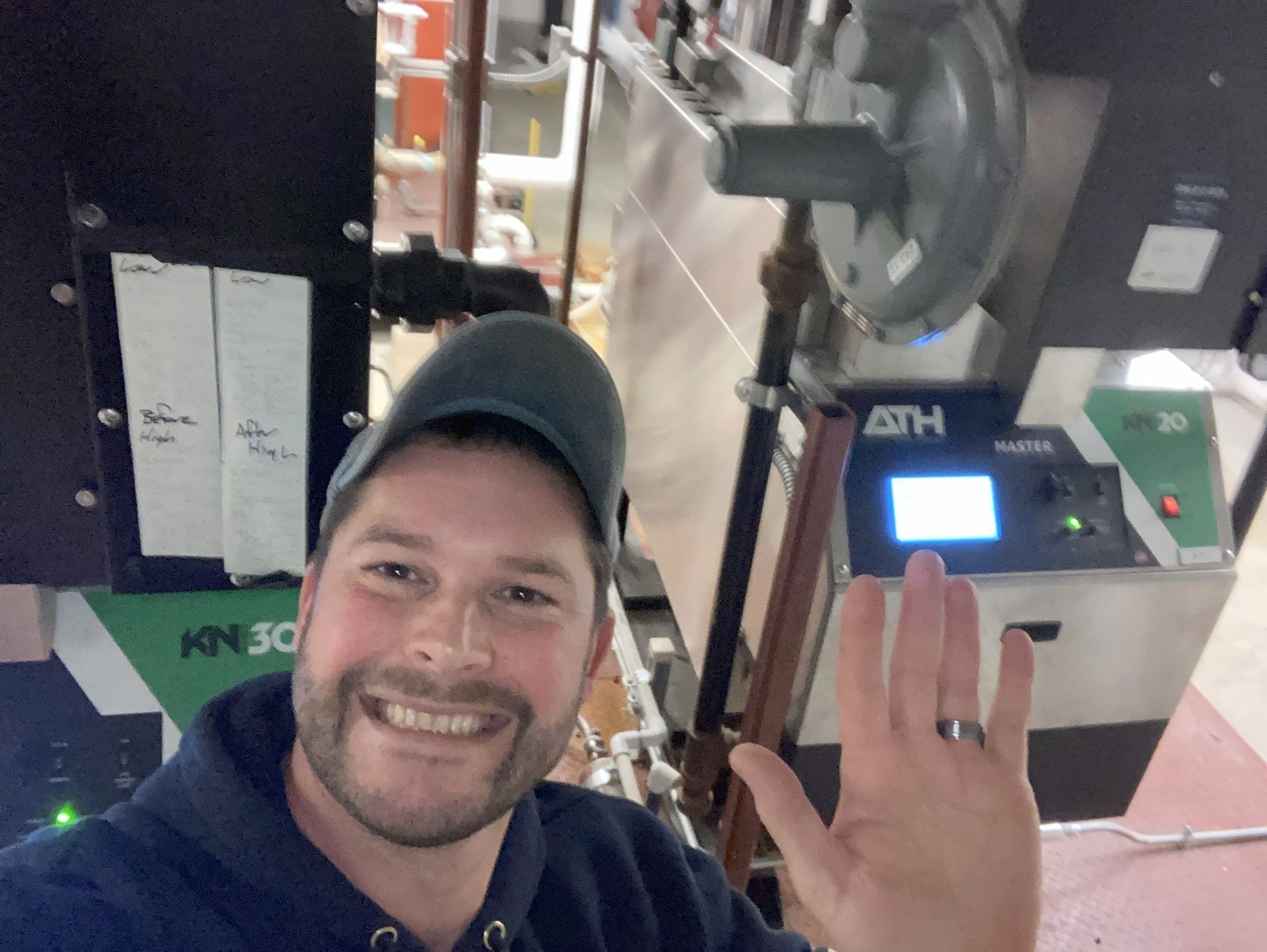 Smiling person waving in front of industrial machinery and a glowing control panel