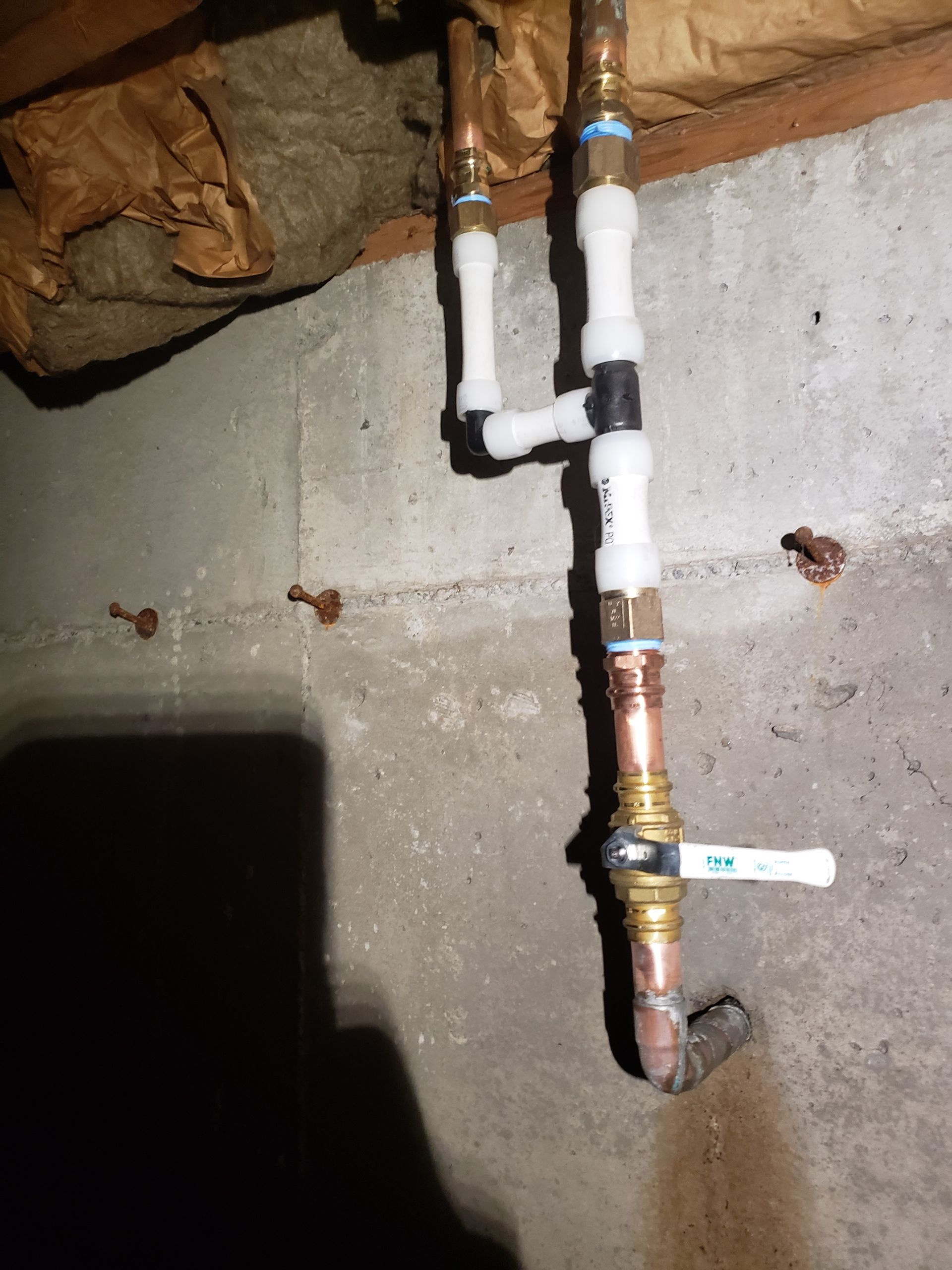 White PVC pipes and a copper pipe on a concrete wall in a basement or crawl space.