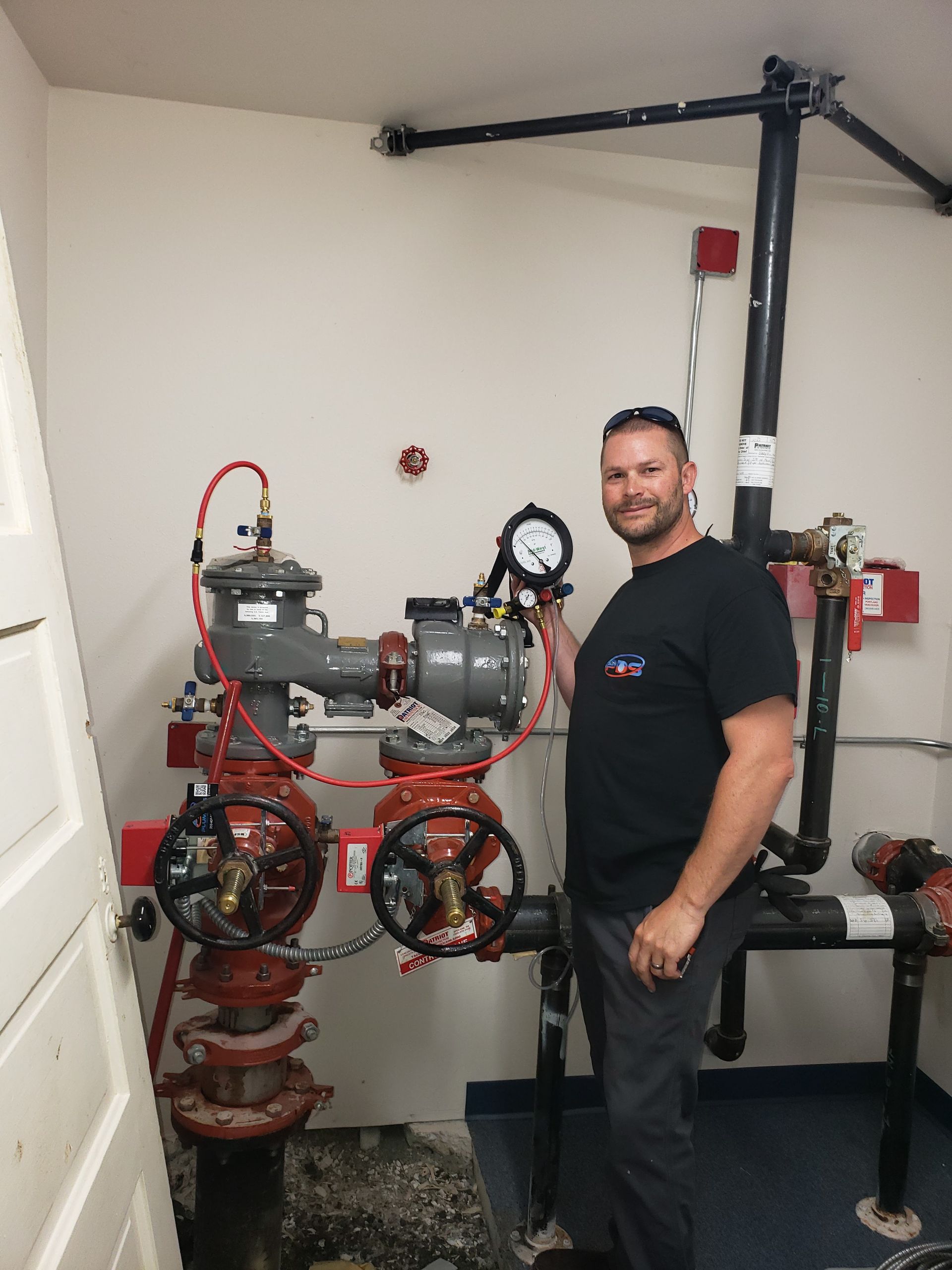 Man standing beside red industrial pipes and gauges in a mechanical room