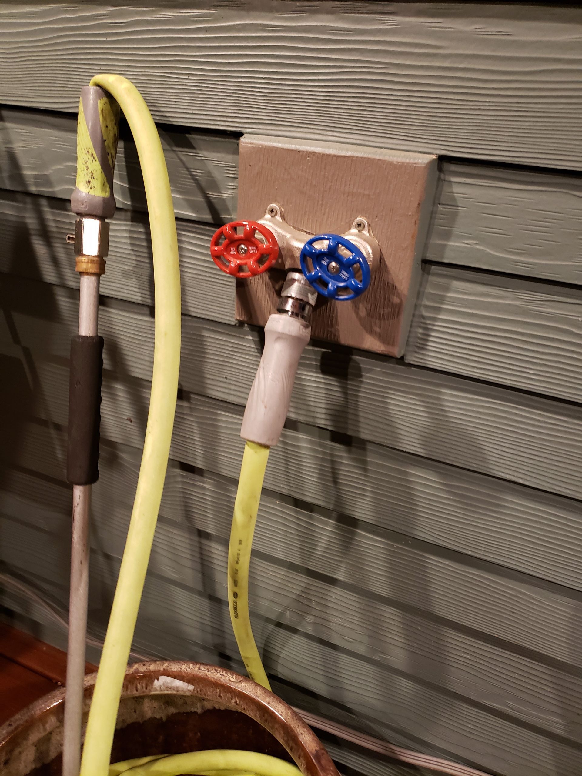 Two outdoor hose bibs with red and blue knobs mounted on a wall, with yellow hoses attached.