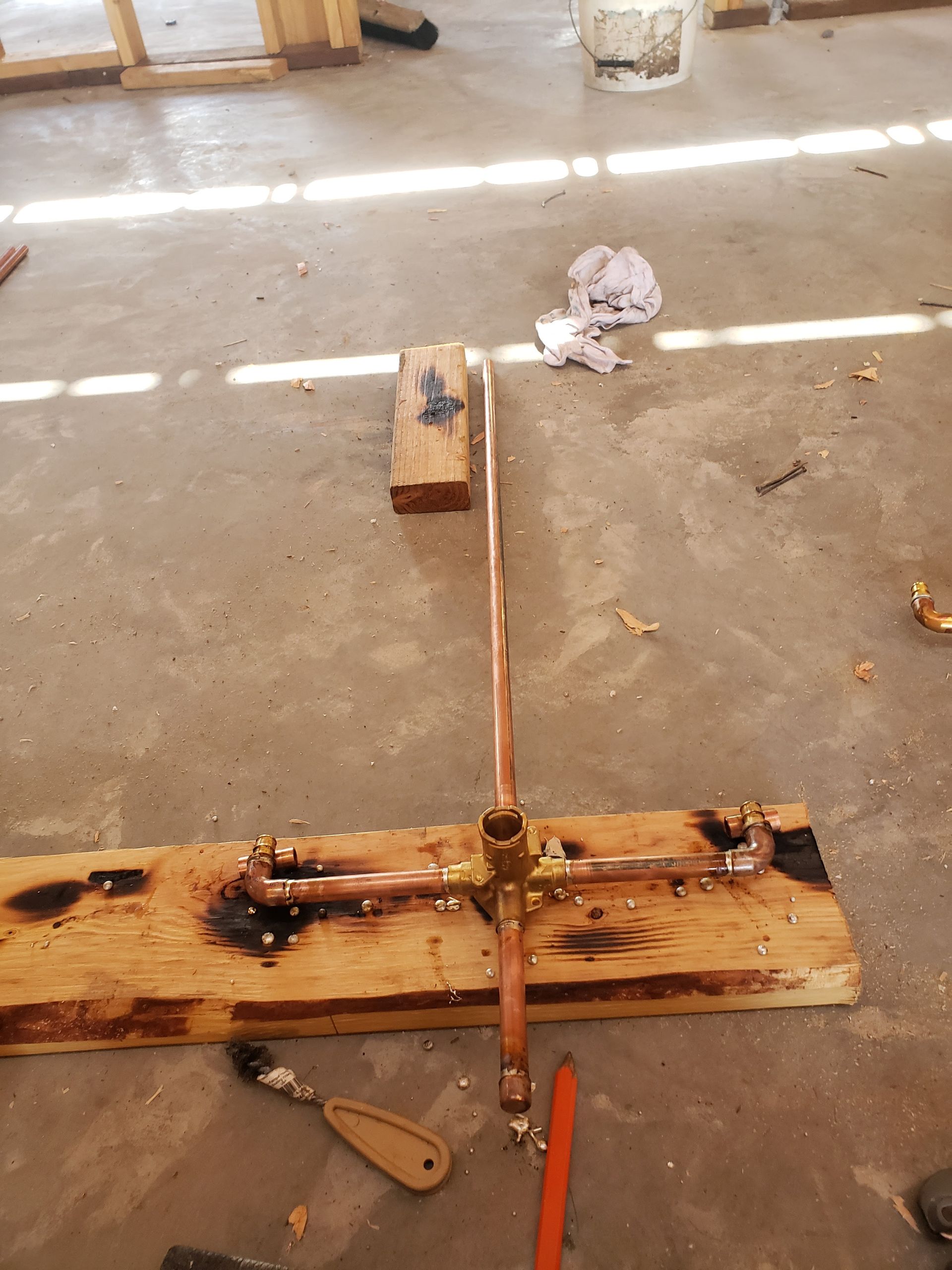 Rusty metal rod and wooden base on a concrete floor in a workshop, with tools nearby.