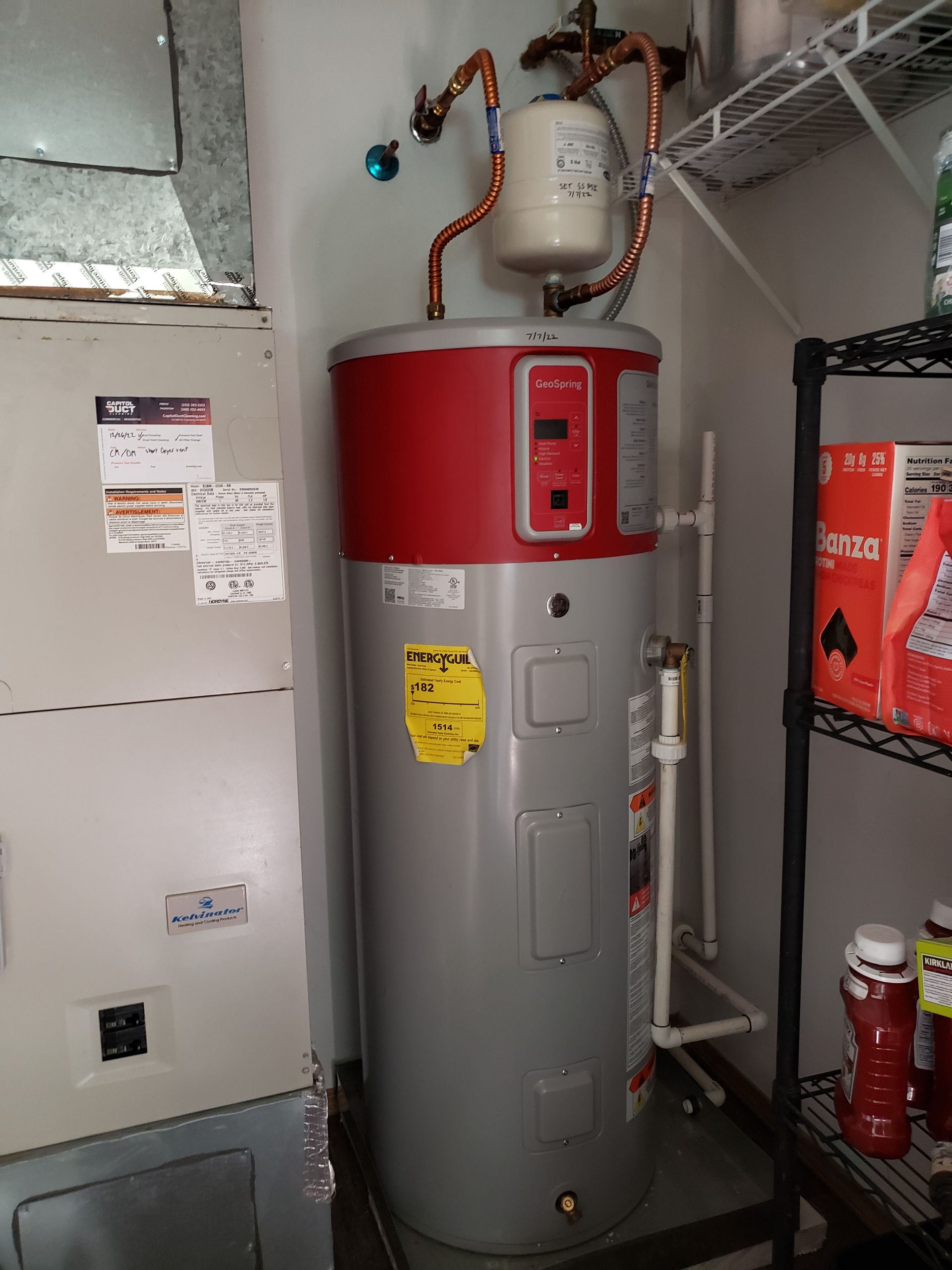 Water heater in a utility closet with a red top, pipes, and a nearby furnace unit.