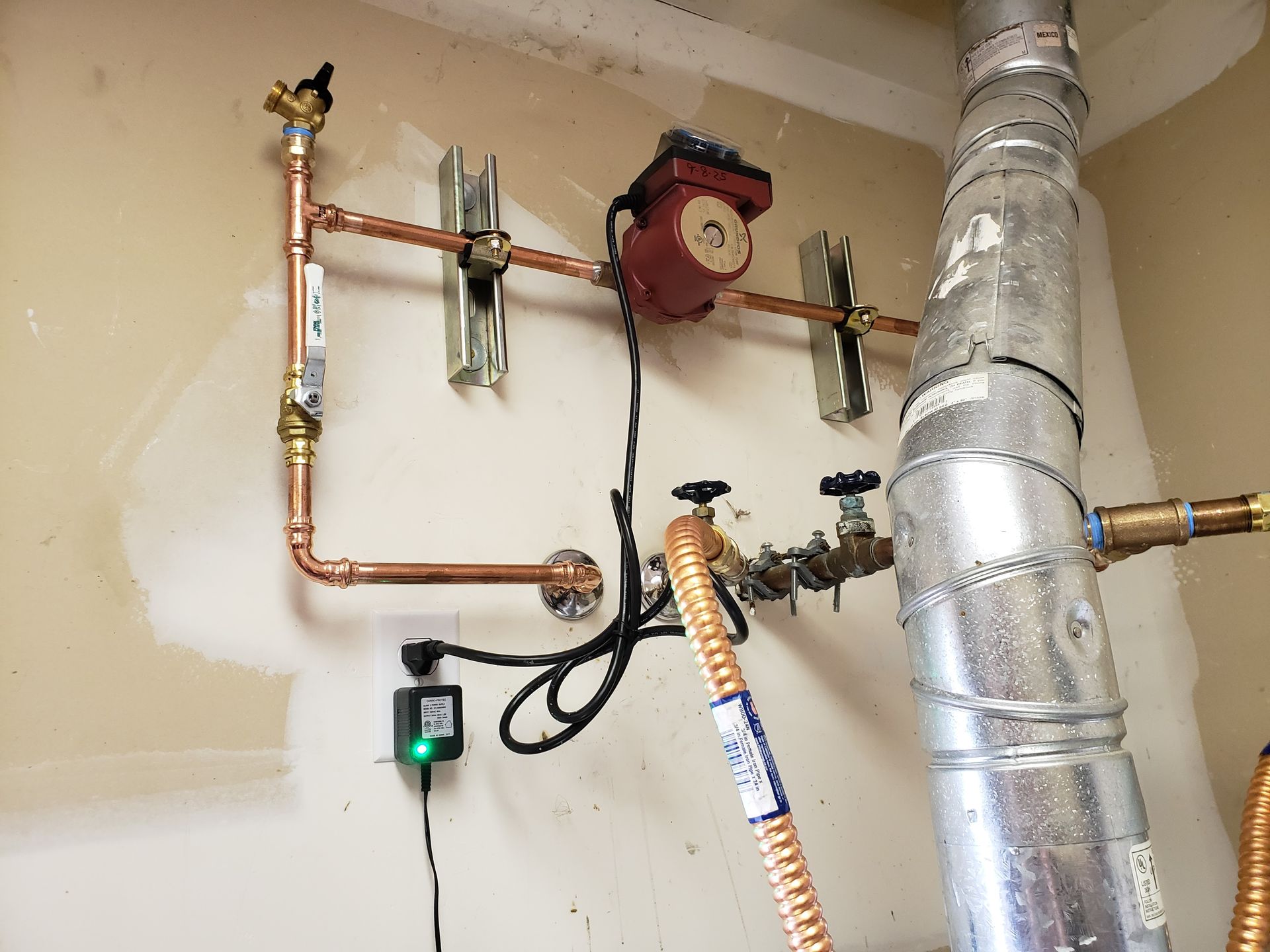 Home utility pipes, pressure gauge, and a large silver HVAC duct in a basement wall.