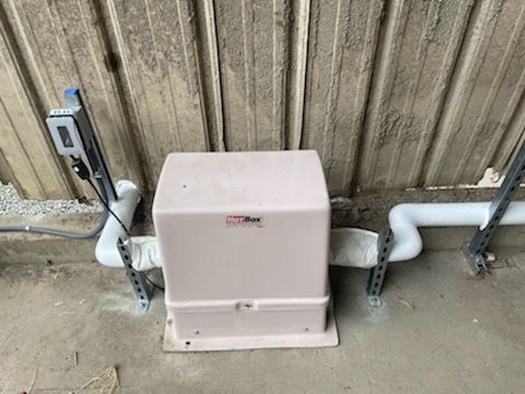White utility box mounted on a concrete floor against a corrugated wall, with electrical conduit and cables nearby