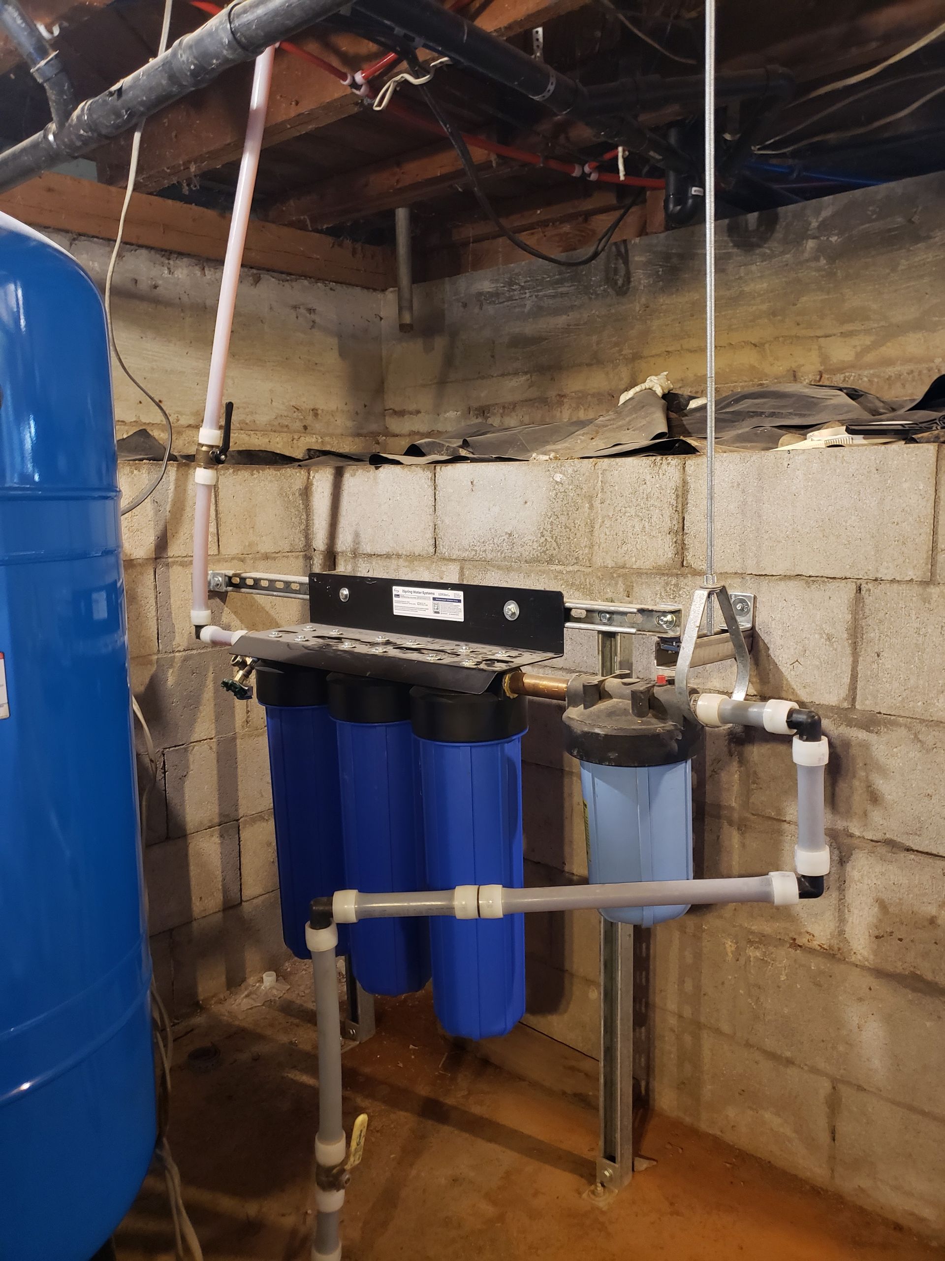 Basement water filtration system with blue tanks, white pipes, and cinder block wall.