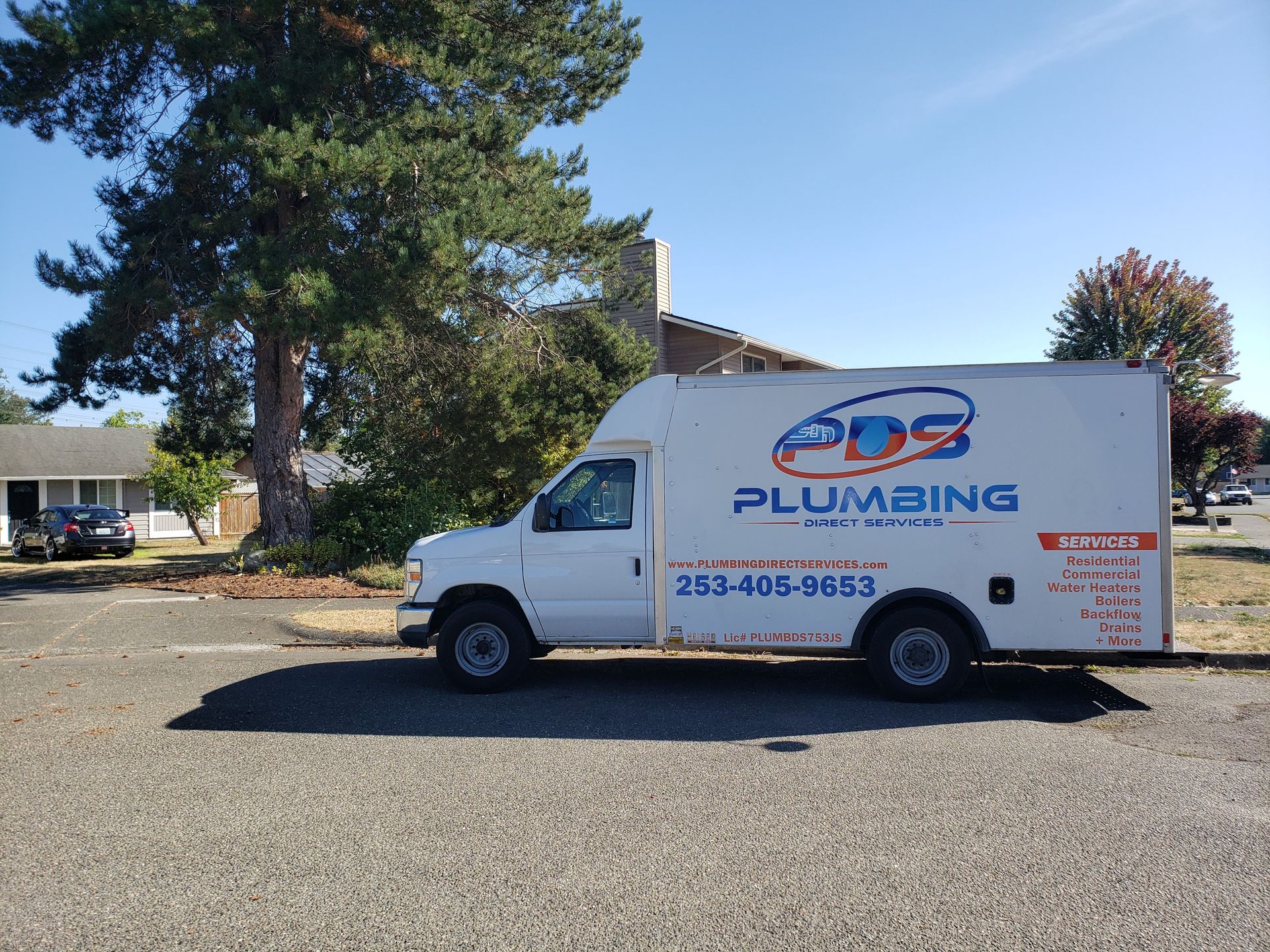White plumbing service van parked outdoors with large trees in the background