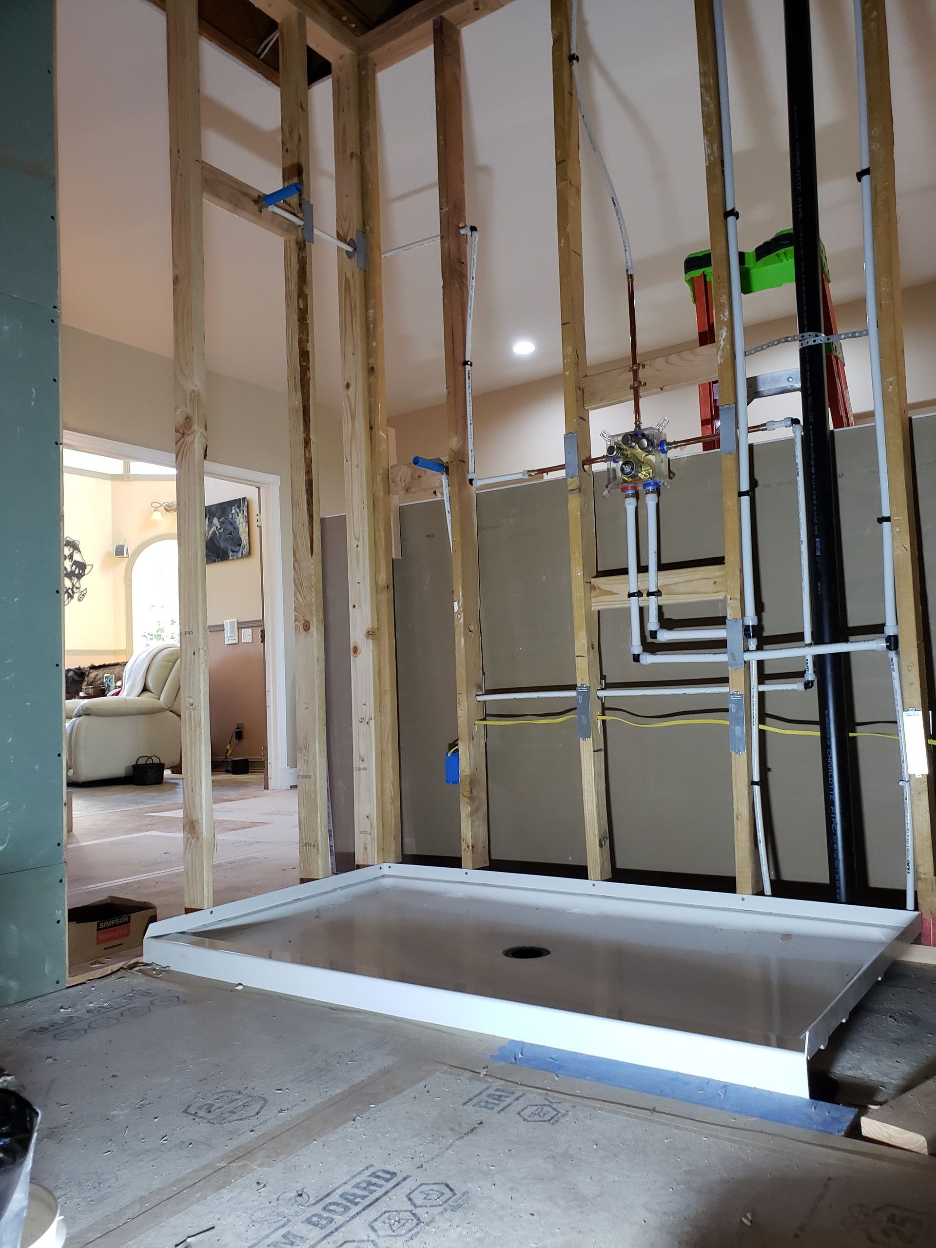 Bathroom under renovation with open wall studs and a partially installed shower base.