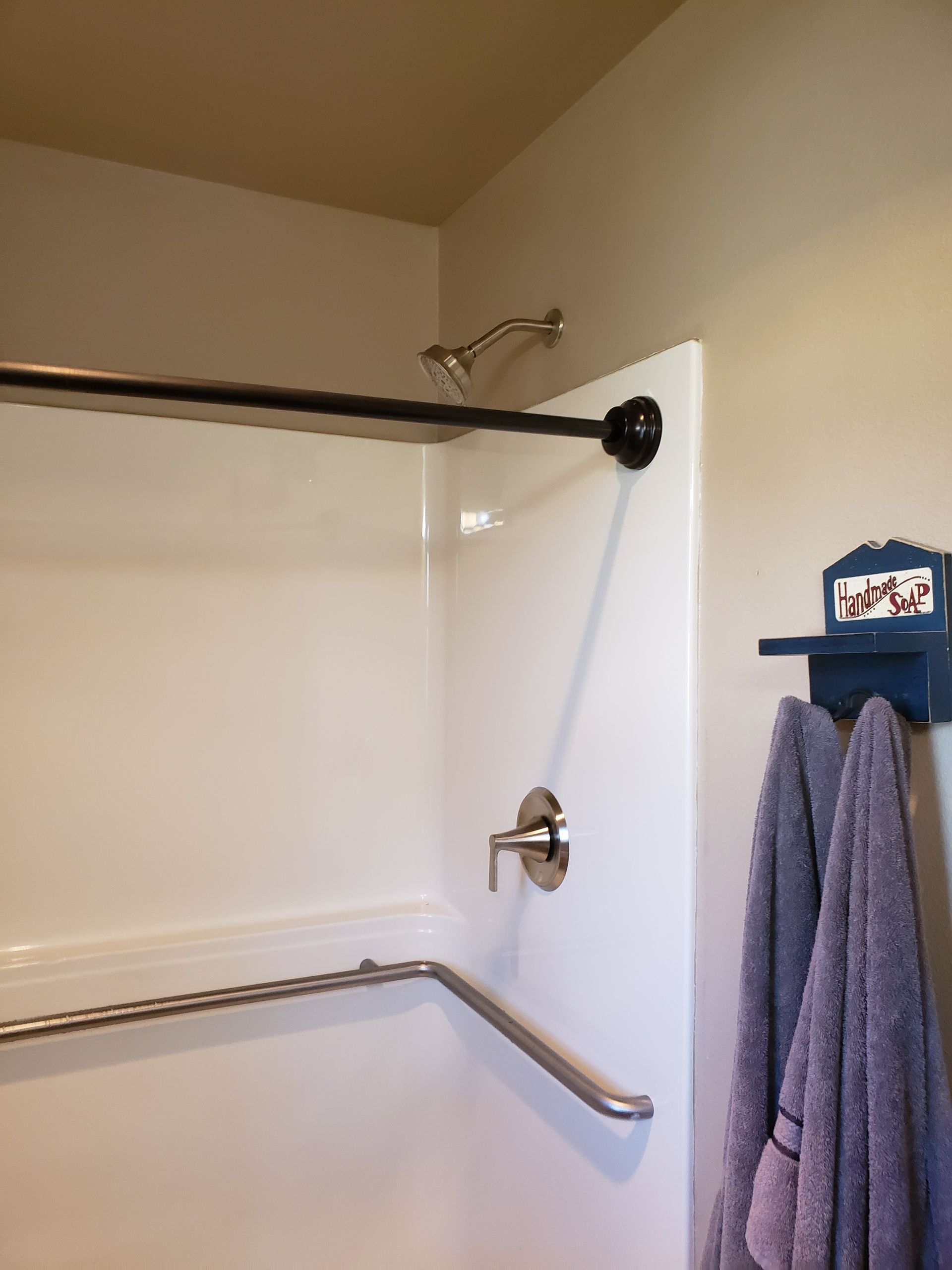 Bathroom shower with white walls, two grab bars, and a blue towel rack with two towels.