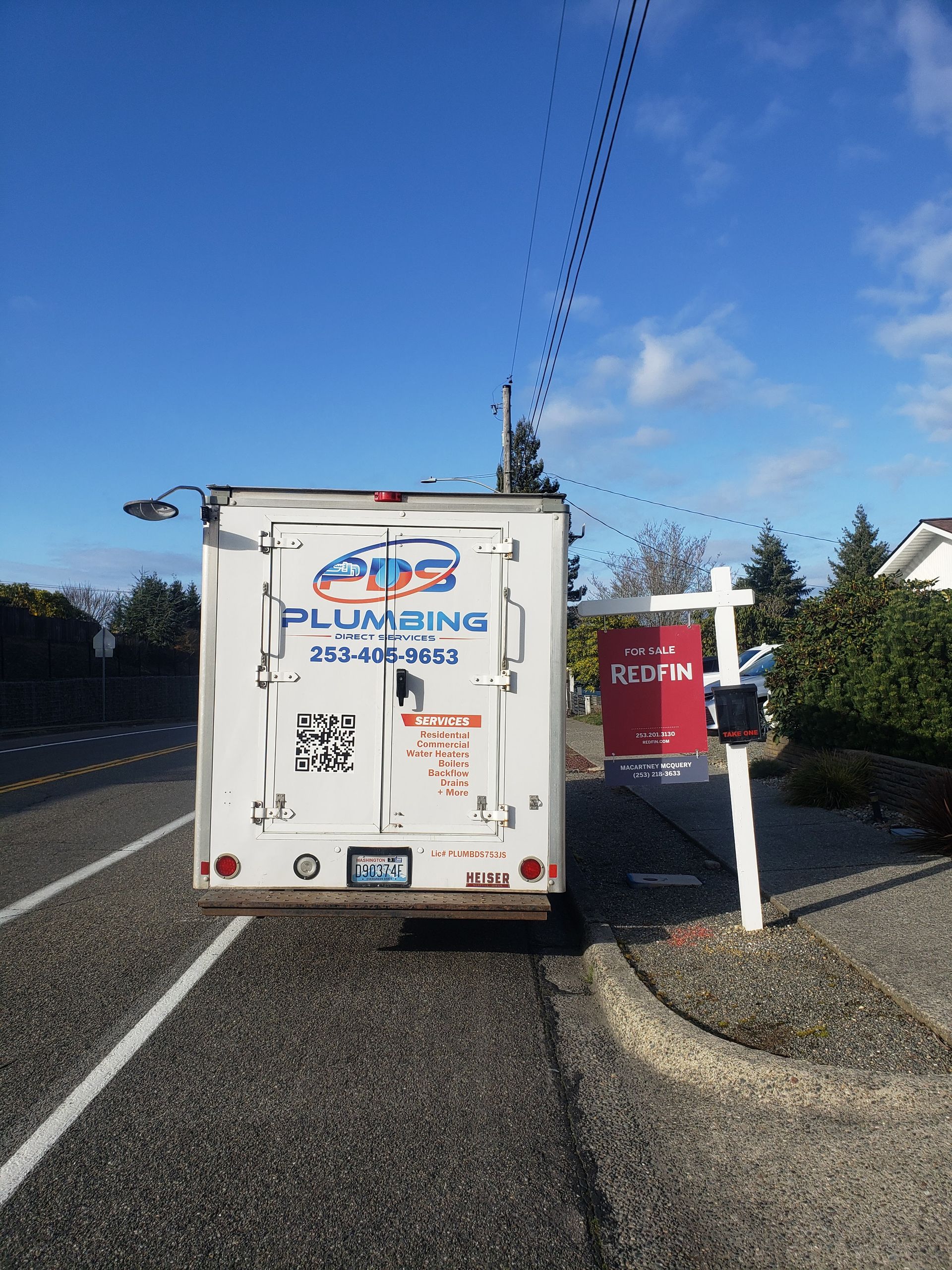 Plumbing truck stopped on a roadside shoulder beside a red mailbox and white house under a blue sky