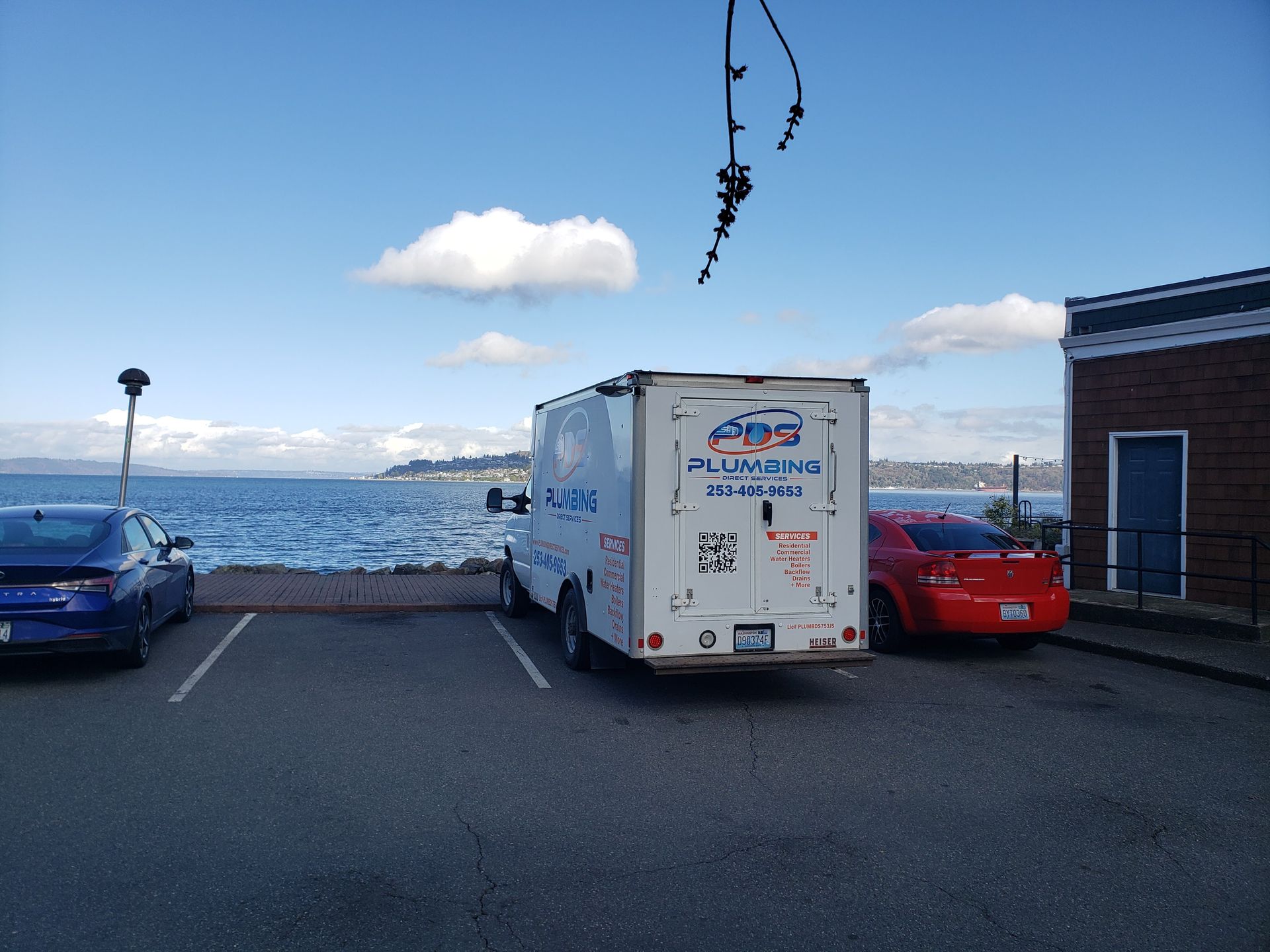 White RV and parked cars beside a waterfront under a blue sky