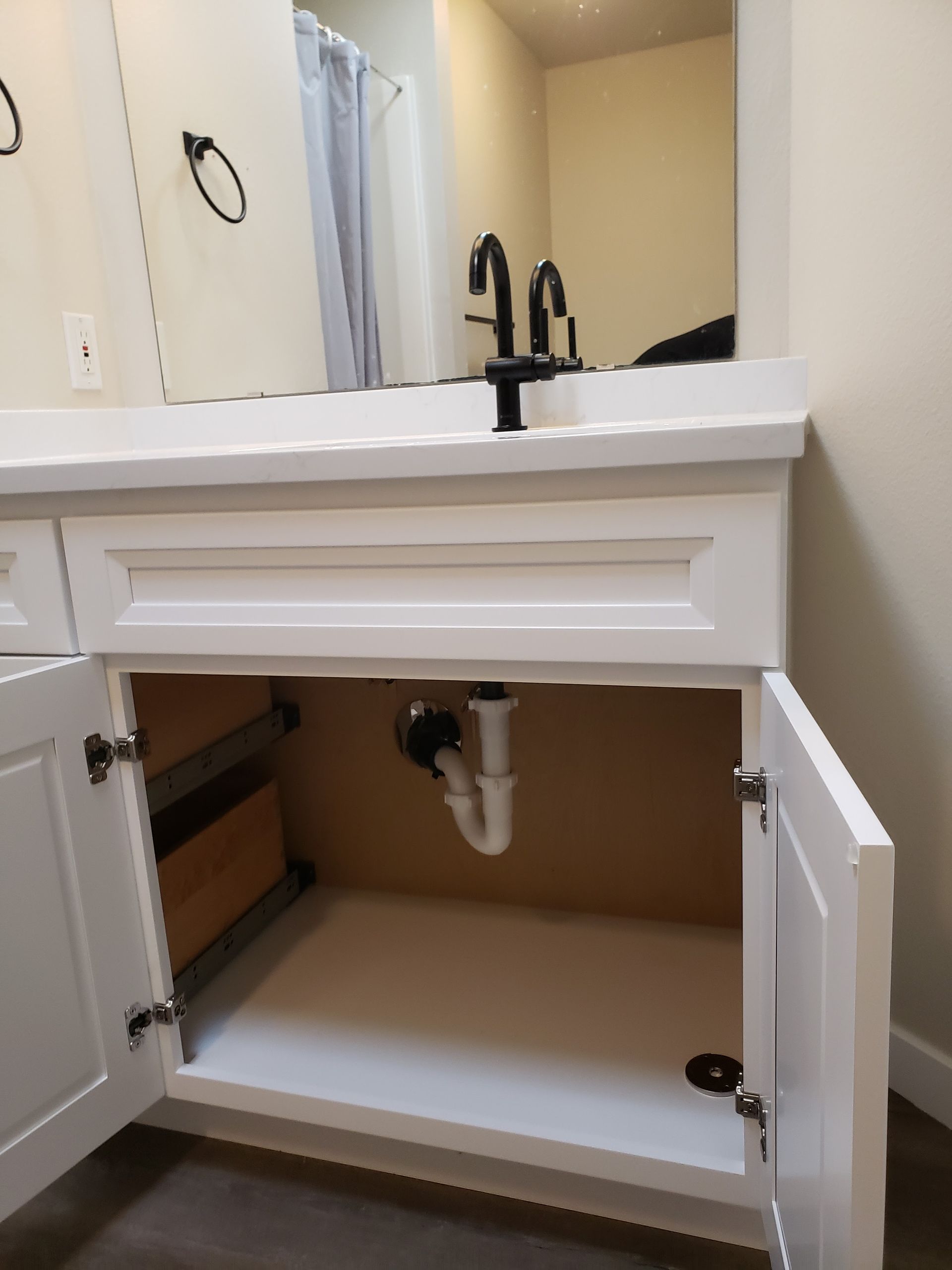 Bathroom vanity with open cabinet doors and visible sink plumbing underneath