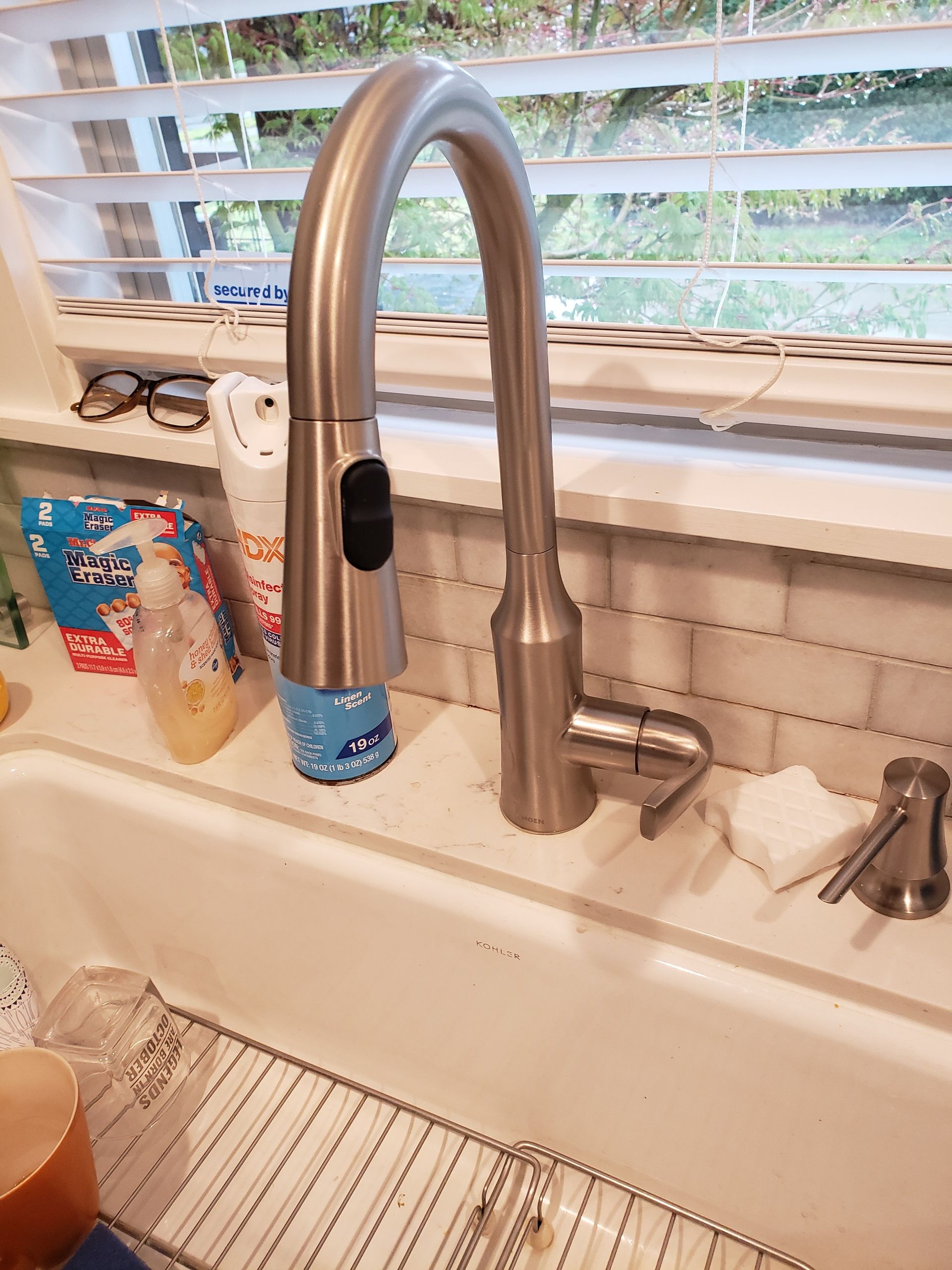 Kitchen sink with high-arc stainless faucet, window blinds, soap dispenser, and dish rack on the counter.