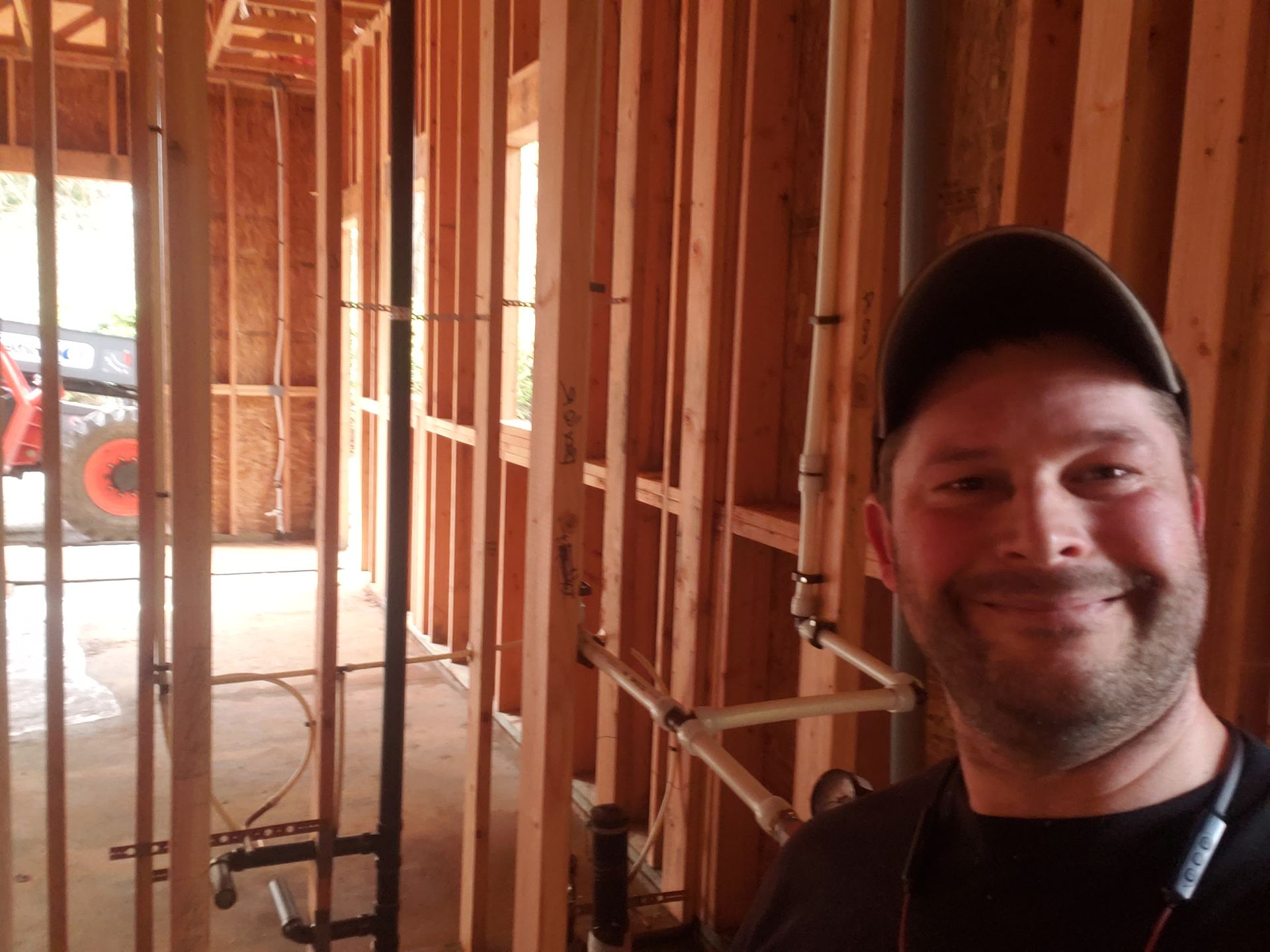 Smiling person in a black cap inside a wood-framed house under construction.