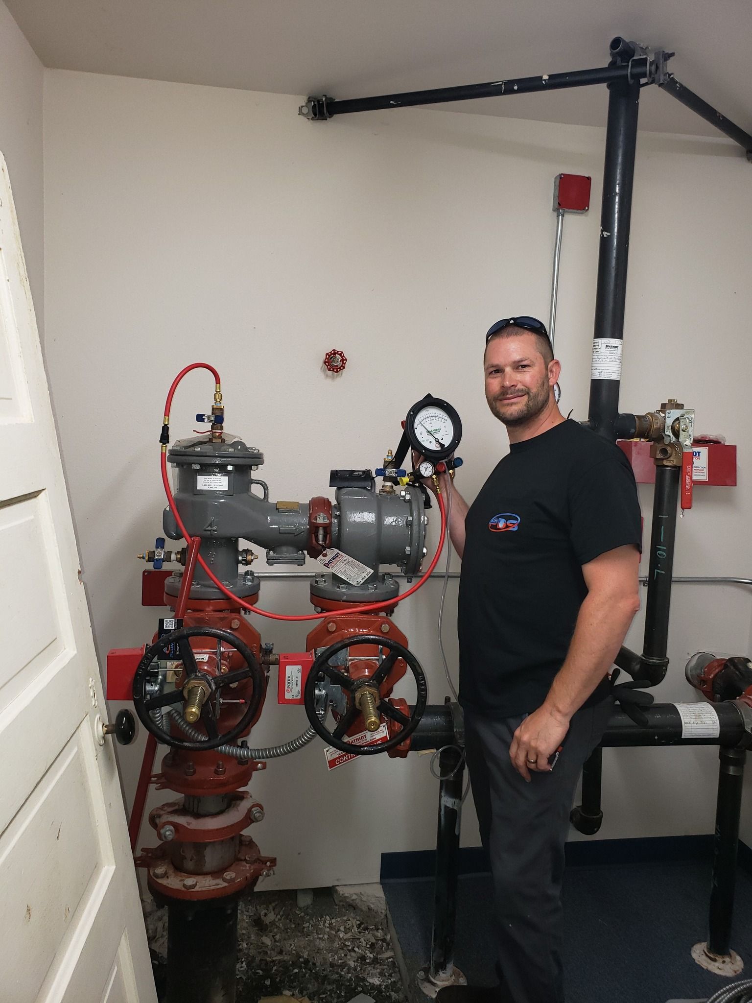 Man standing beside red industrial pumps and gauges in a utility room