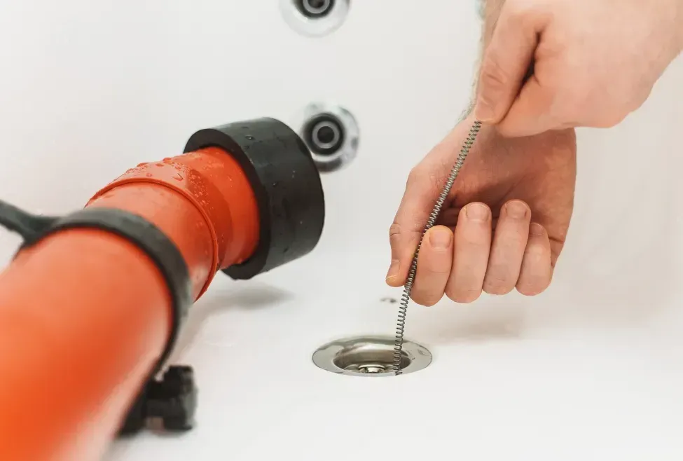 Hand holding a chain plug near a metal sink drain with an orange pipe on the left