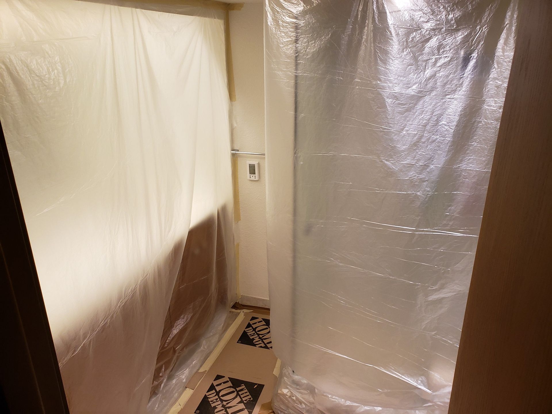 Plastic-covered doorway and hallway under renovation, with protective sheeting on walls and floor.