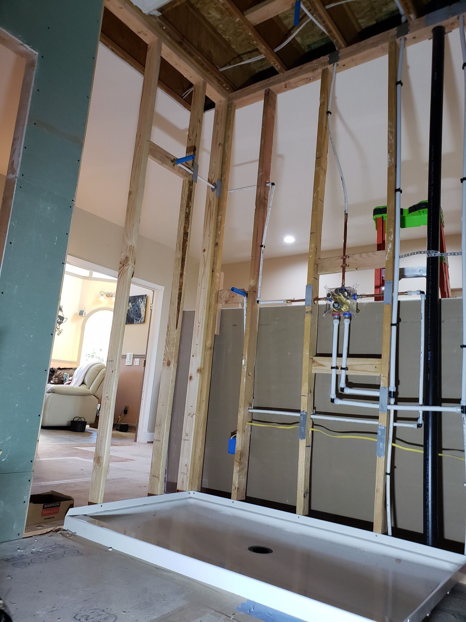 Framed interior wall under renovation with exposed studs, plumbing, and a bathtub alcove.