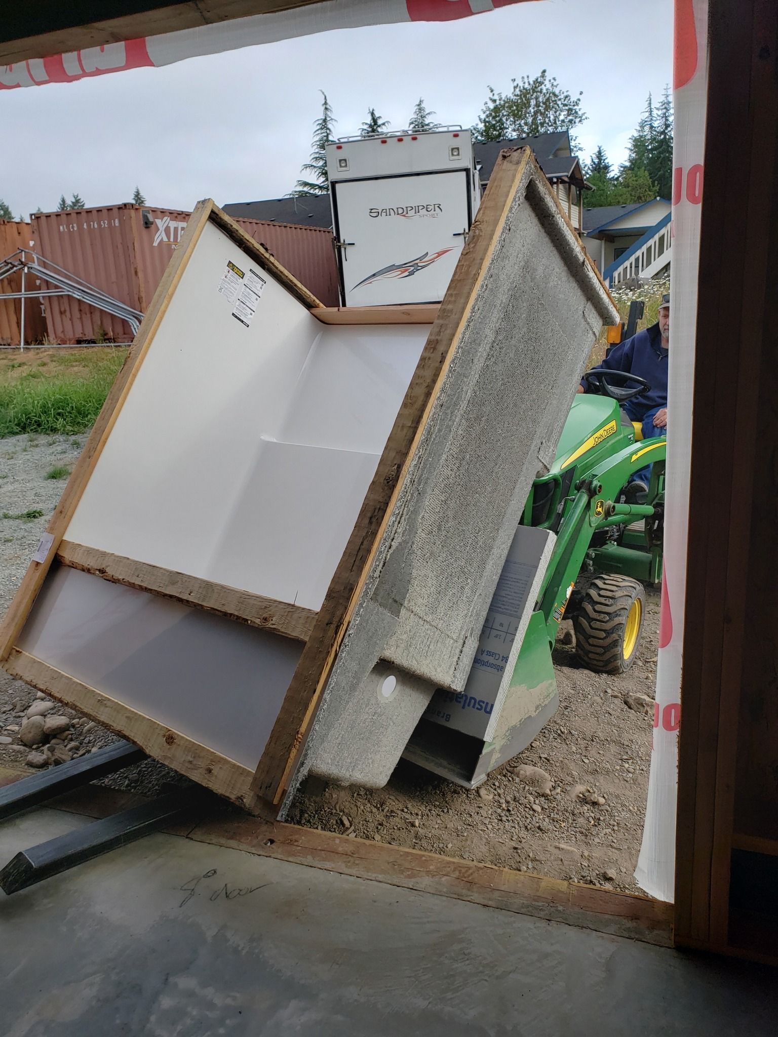 Leaning wooden cabinet parts and debris at a worksite or garage opening, with a green machine in the background