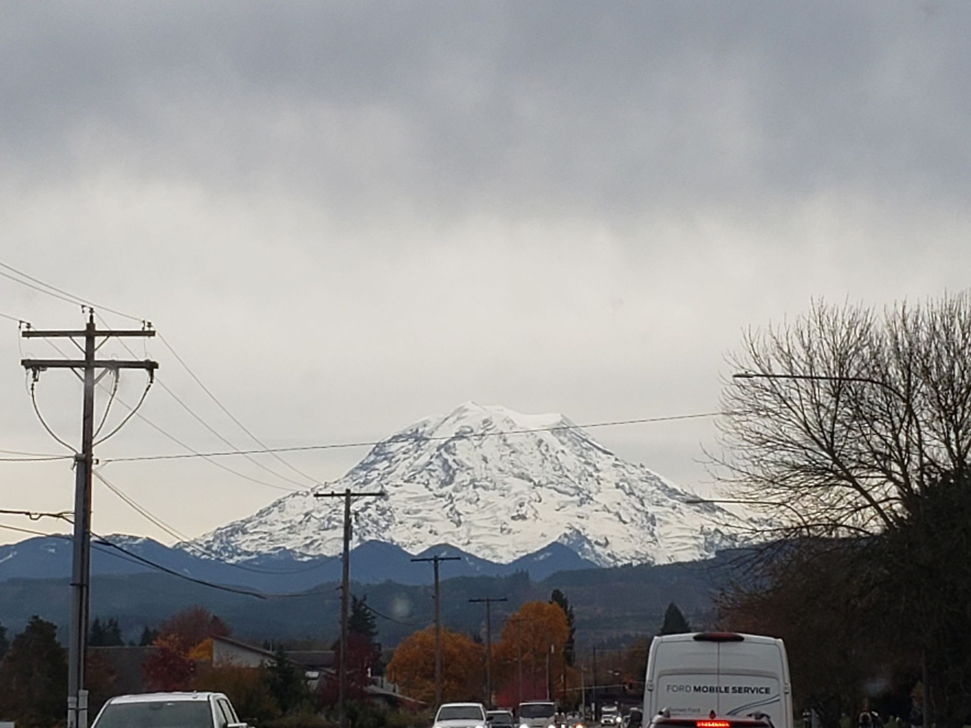 Snow-covered mountain in the distance under a cloudy sky, with power lines and a road in the foreground.