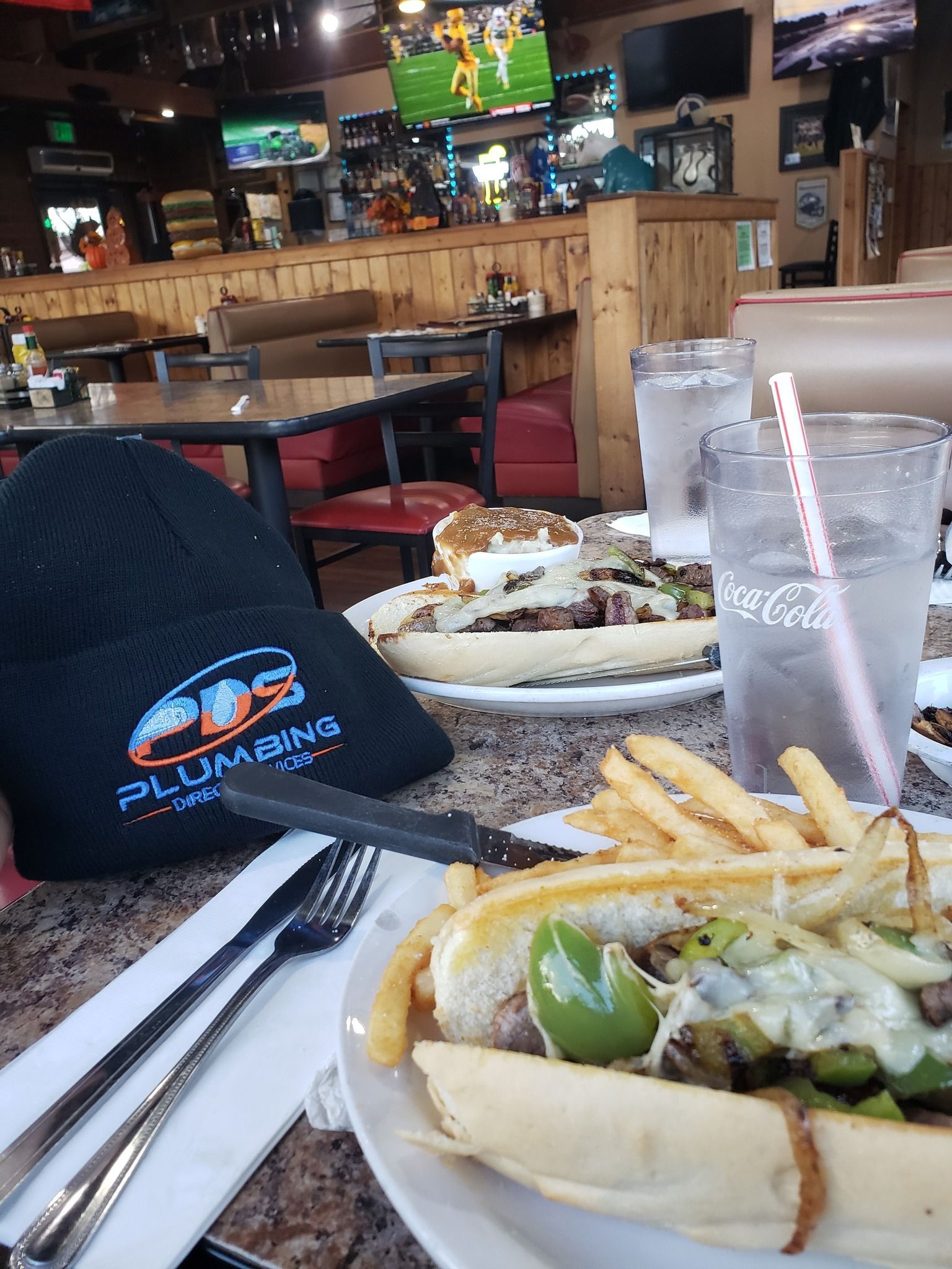 Restaurant table with hot dogs, fries, drinks, and a black cap in a casual bar setting