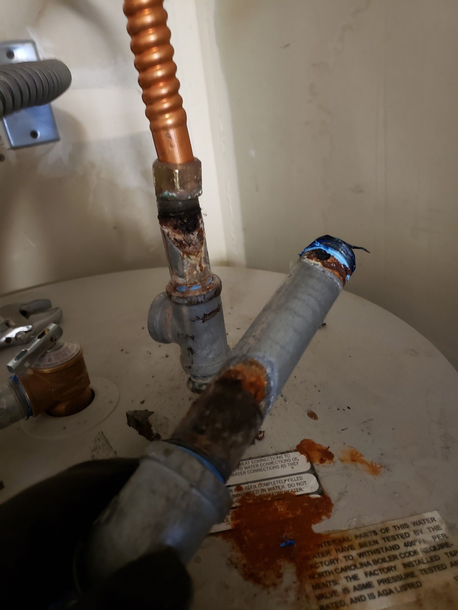 Corroded plumbing pipes under a sink with rust and water damage on the cabinet floor