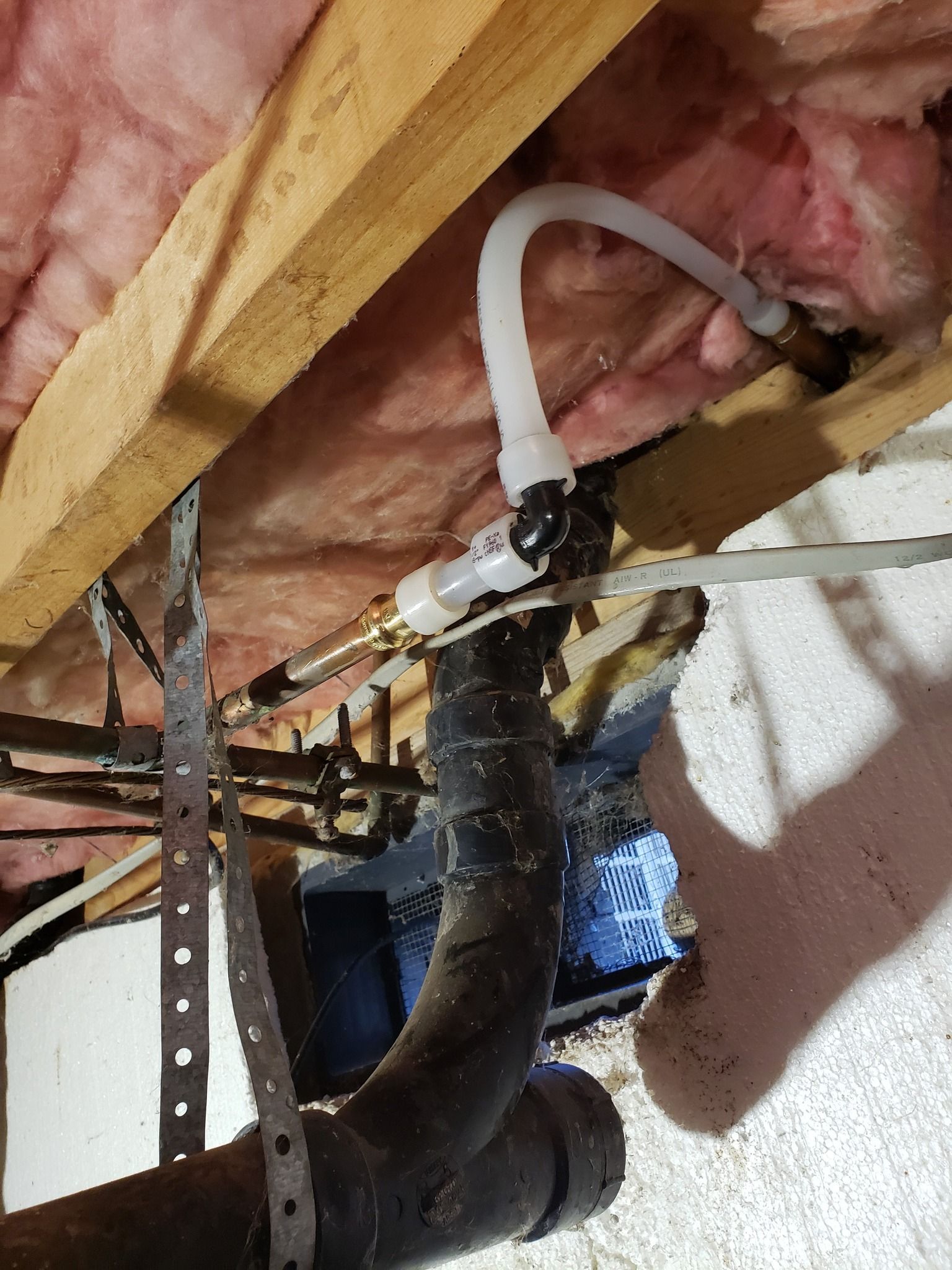 Plumbing pipes and a valve beneath pink insulation in a utility crawlspace