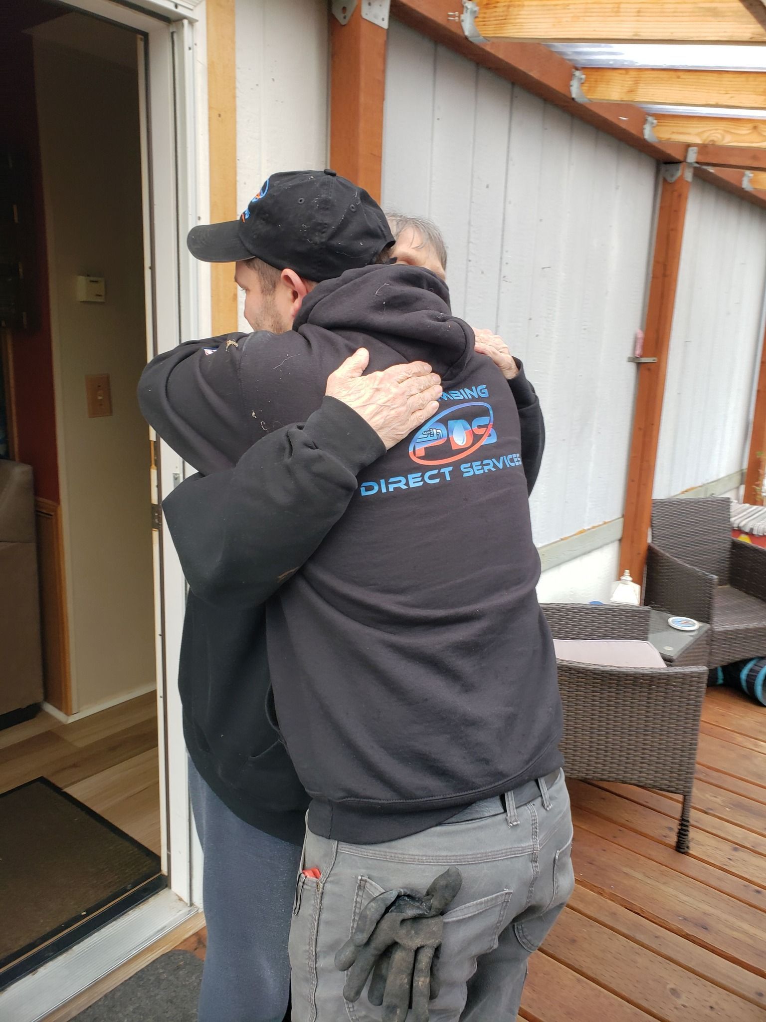 Two people hugging on a wooden deck outside a doorway