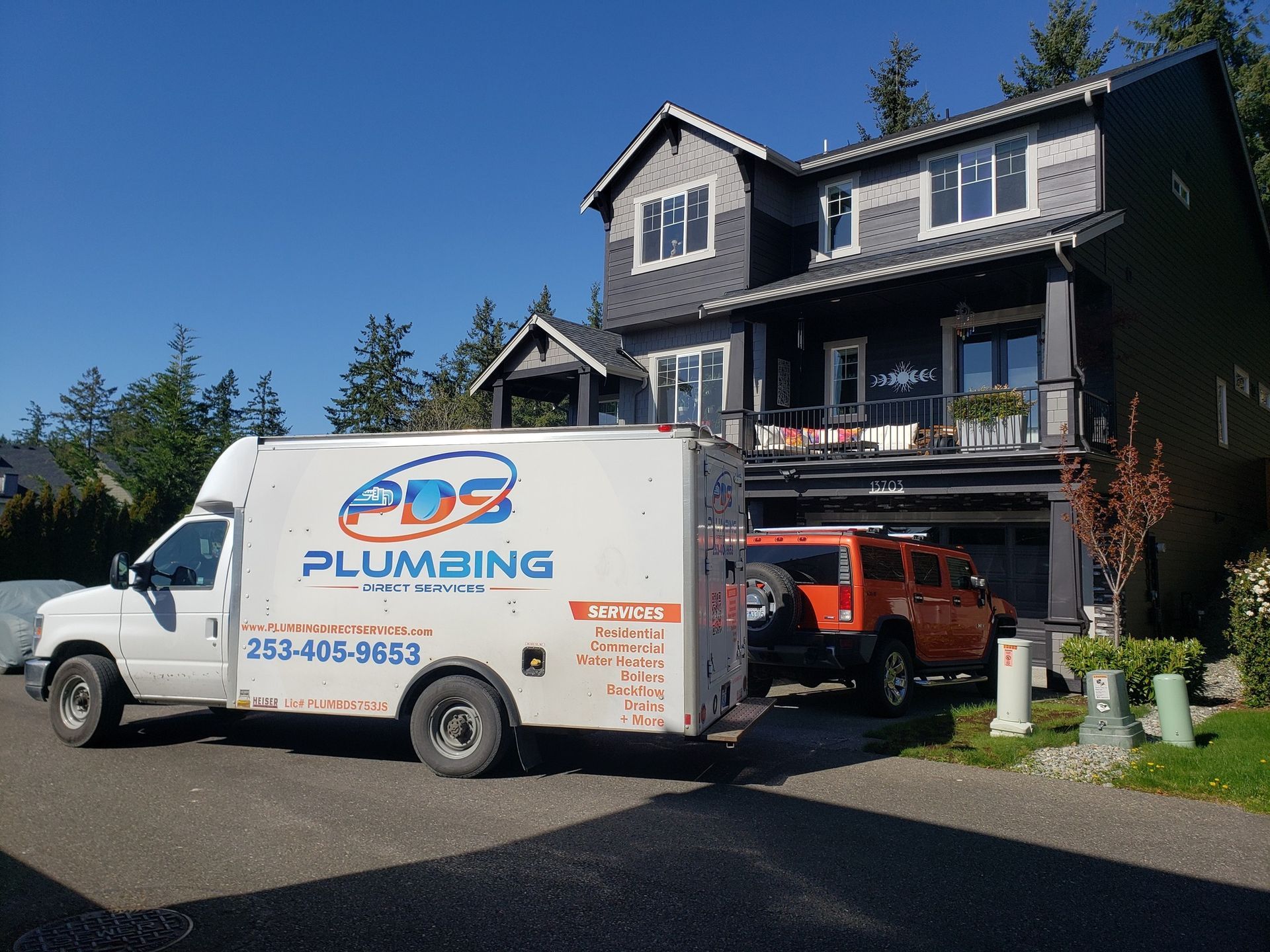 White plumbing service van parked in driveway beside a dark house on a sunny day