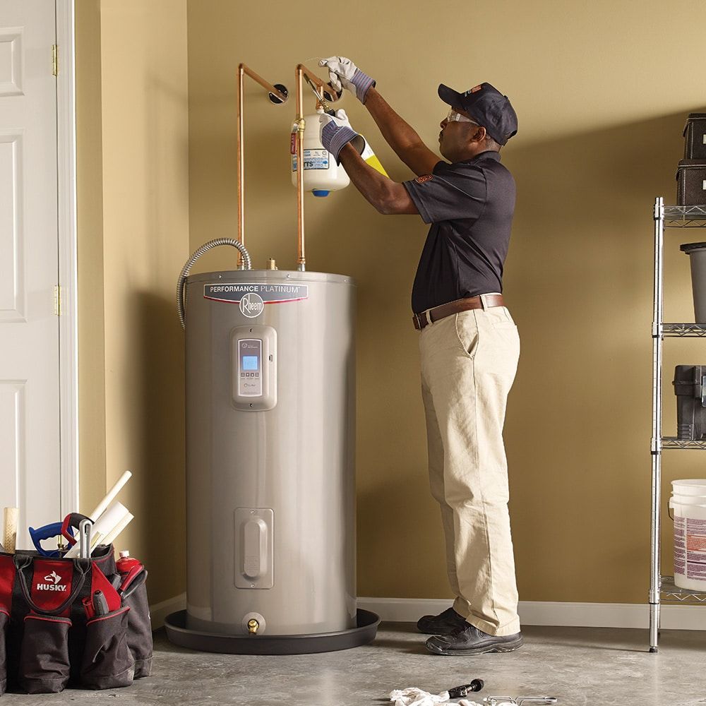 Technician installing a water heater in a garage, using a tool on the top pipe.
