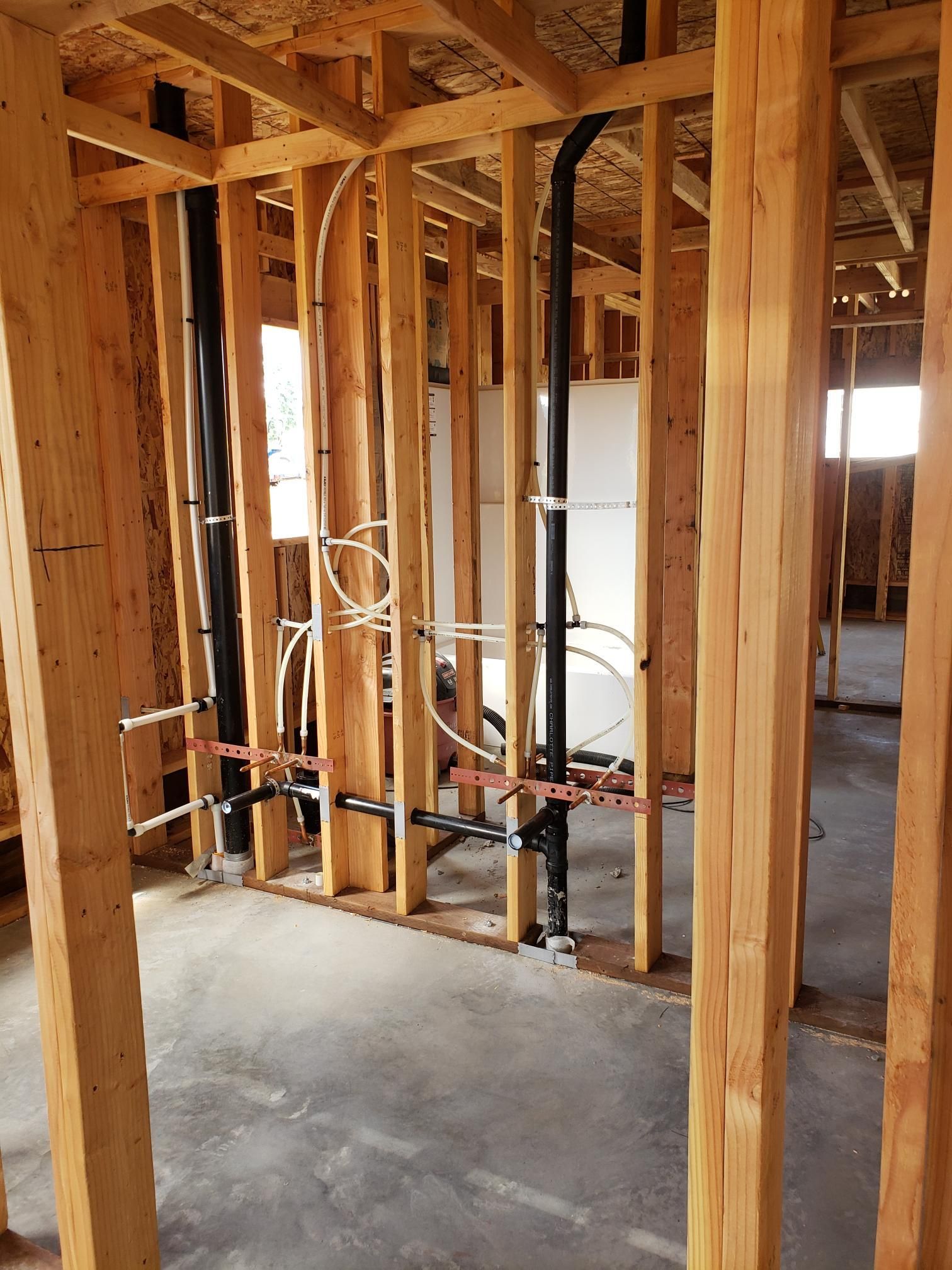 Framed interior wall under construction with exposed wood studs, wiring, and concrete floor.