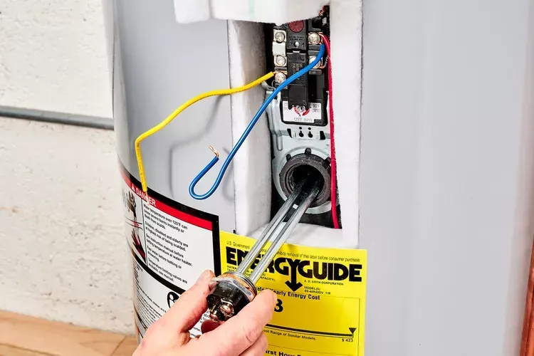 Hand connecting wires in an open water heater control panel with a yellow guide label.