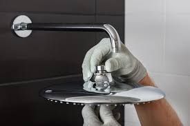 Gloved hands install a chrome shower head on a wall-mounted pipe.
