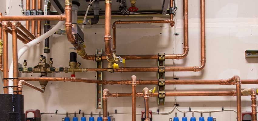 Orange industrial pipes with valves and gauges against a gray wall