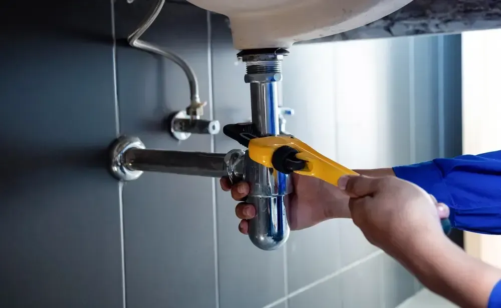 Hand using a yellow wrench to tighten a chrome sink drain pipe under a bathroom sink