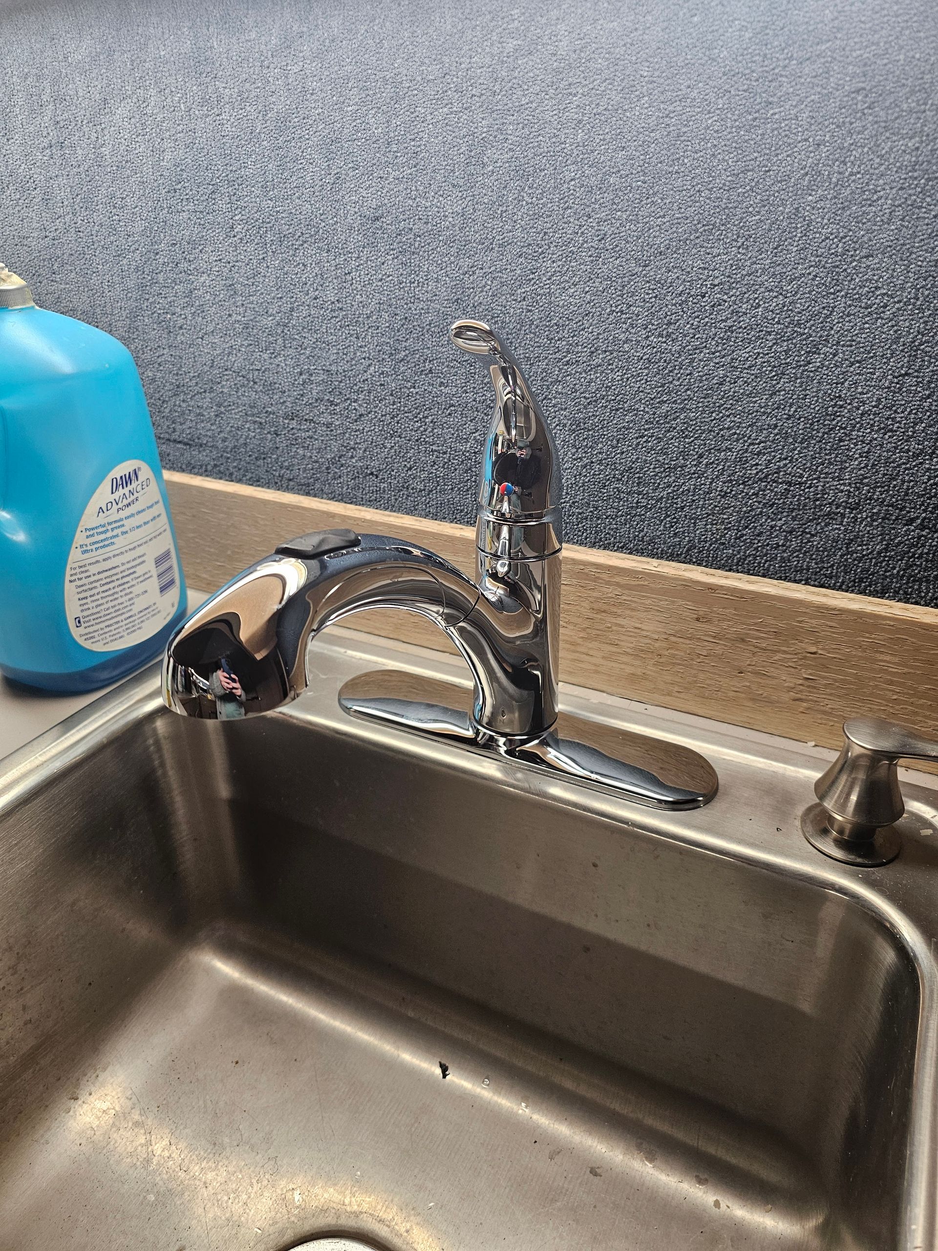 Kitchen sink with chrome faucet, blue soap bottle, and speckled backsplash in a countertop setting
