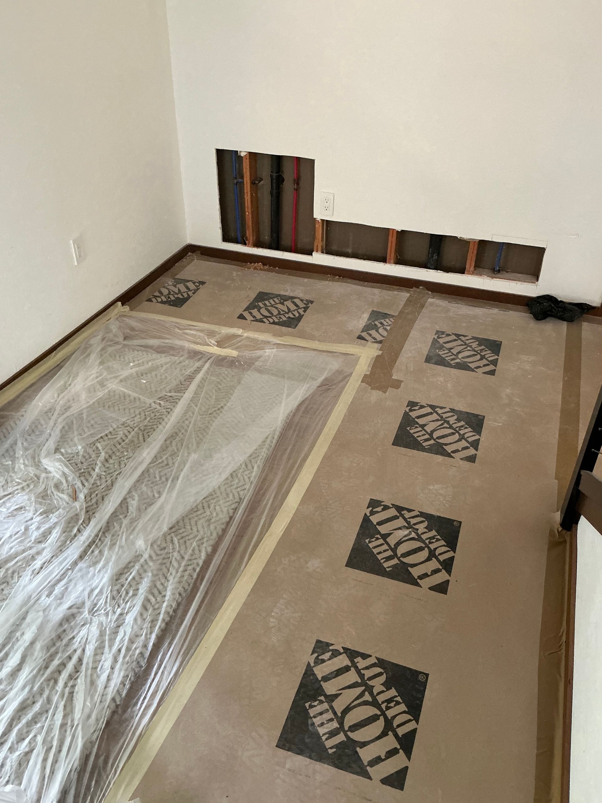Partially covered floor in an unfinished room with beige carpet tiles and stacked boards along the wall