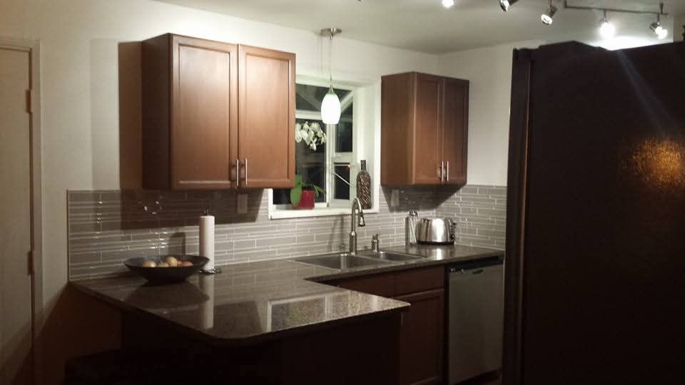 Modern kitchen with dark countertops, wood cabinets, a sink, stove, and refrigerator under track lighting