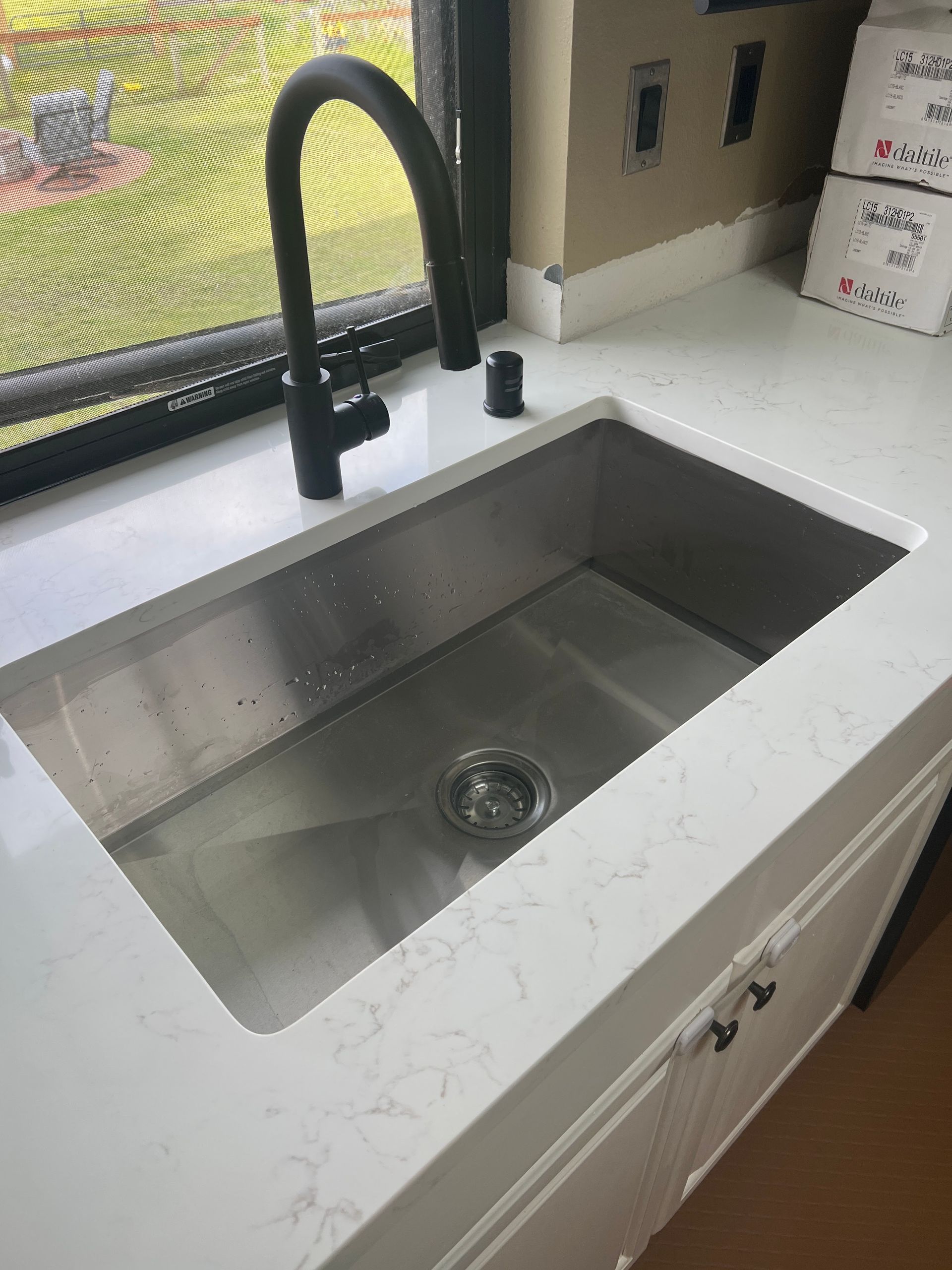 Stainless steel kitchen sink under a black faucet on a white countertop by a window.